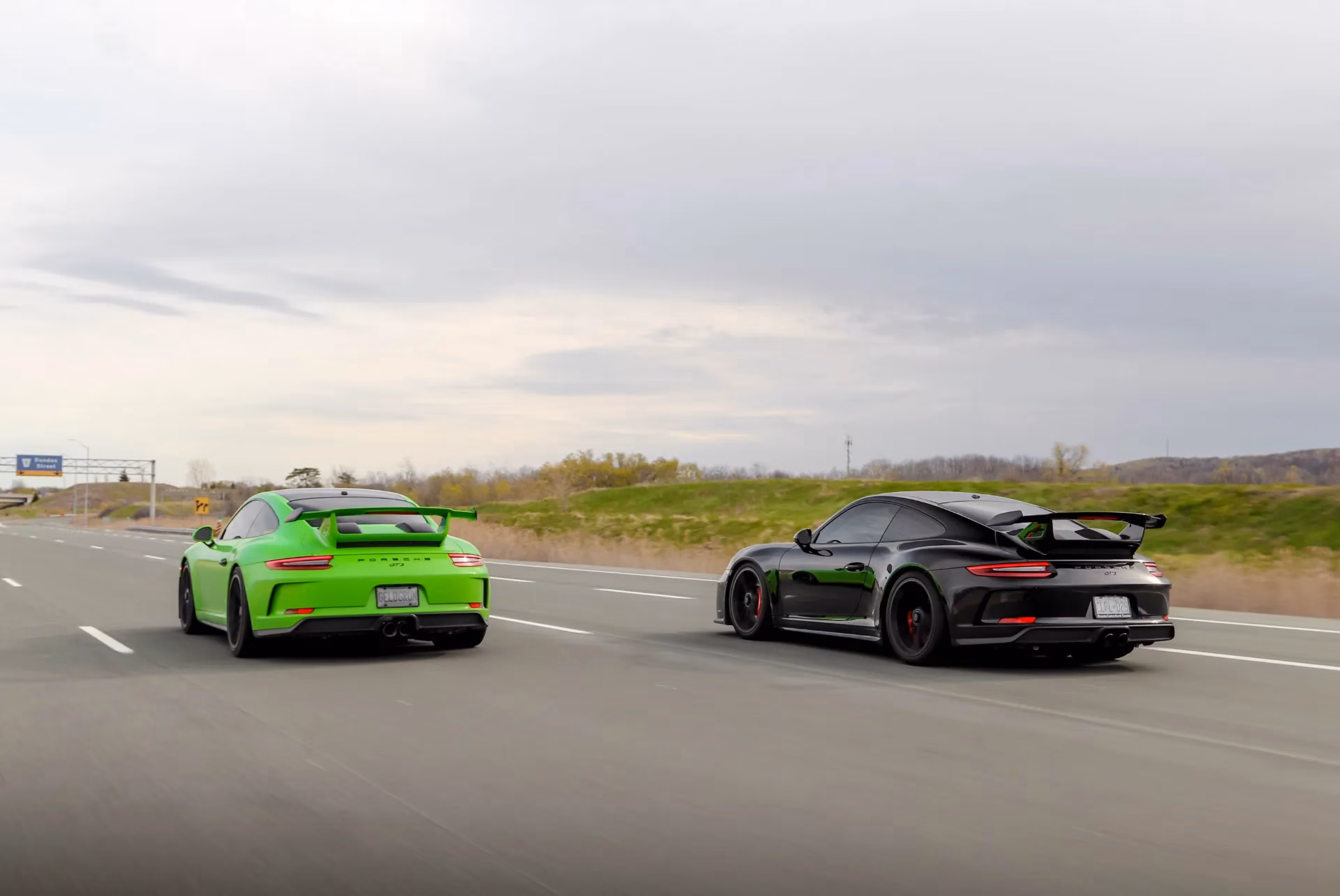 A lime green and a black Porsche 911 driving side by side on the highway