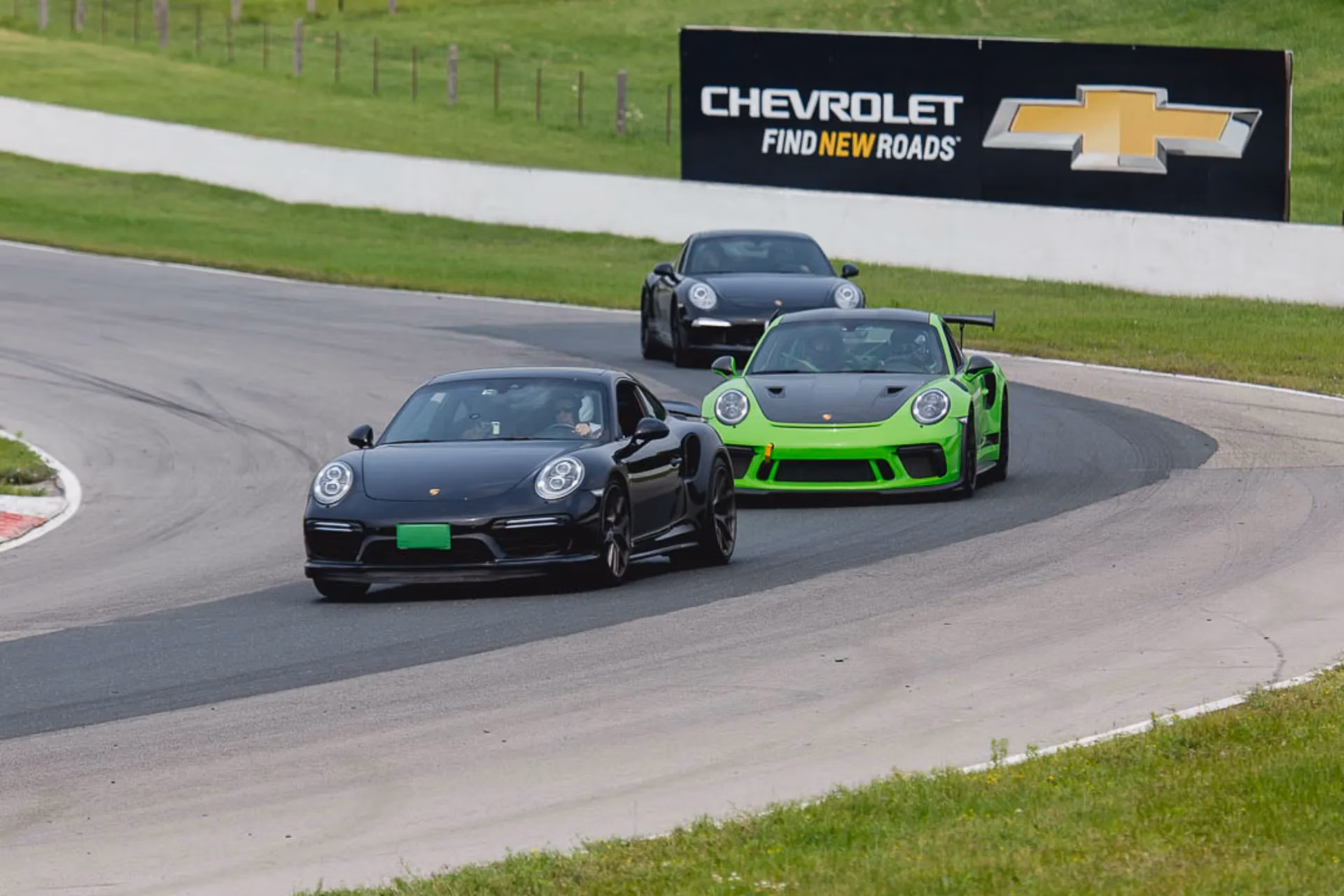 A black, a lime green and a dark Porsche 911 cornering together on track