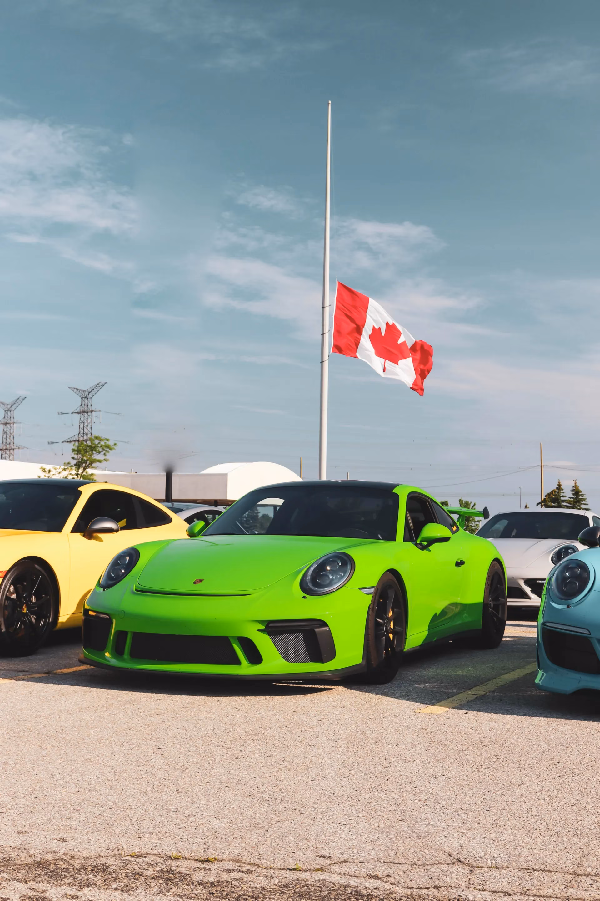 A lime green Porsche 911 parked beneath a Canadian flag, yellow and blue Porsches alongside