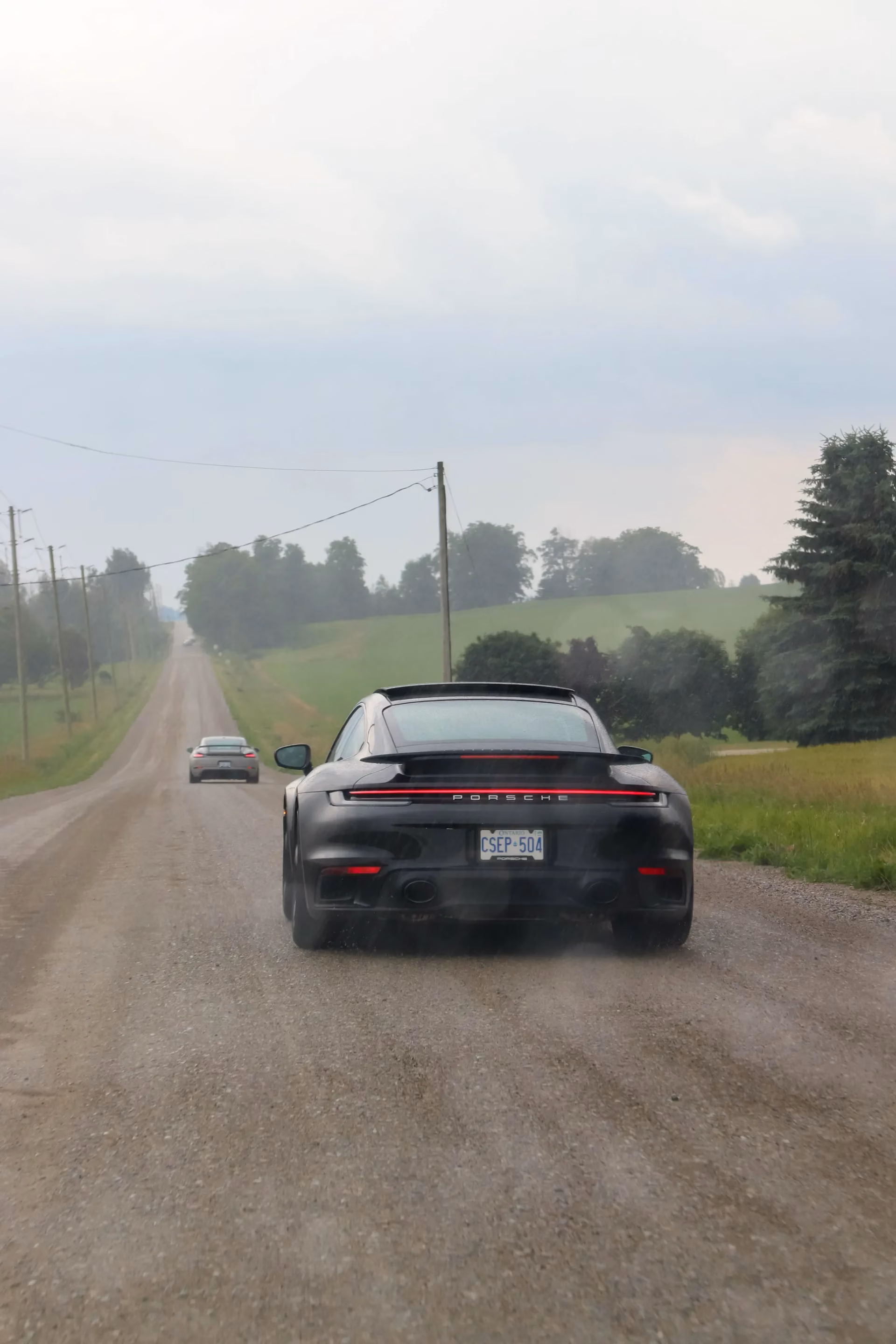 A black Porsche 911 raising dust on a gravel country road