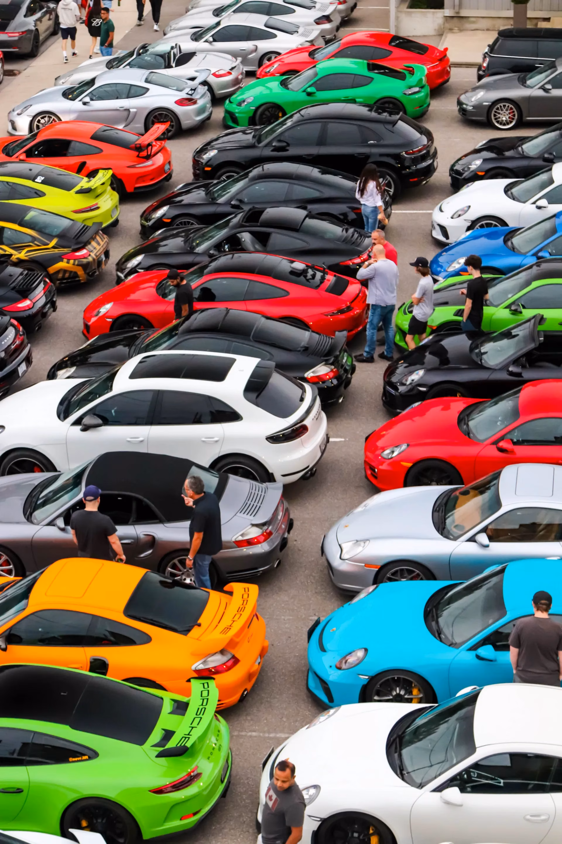Overhead view of a parking lot packed with colourful Porsches, members walking between the rows