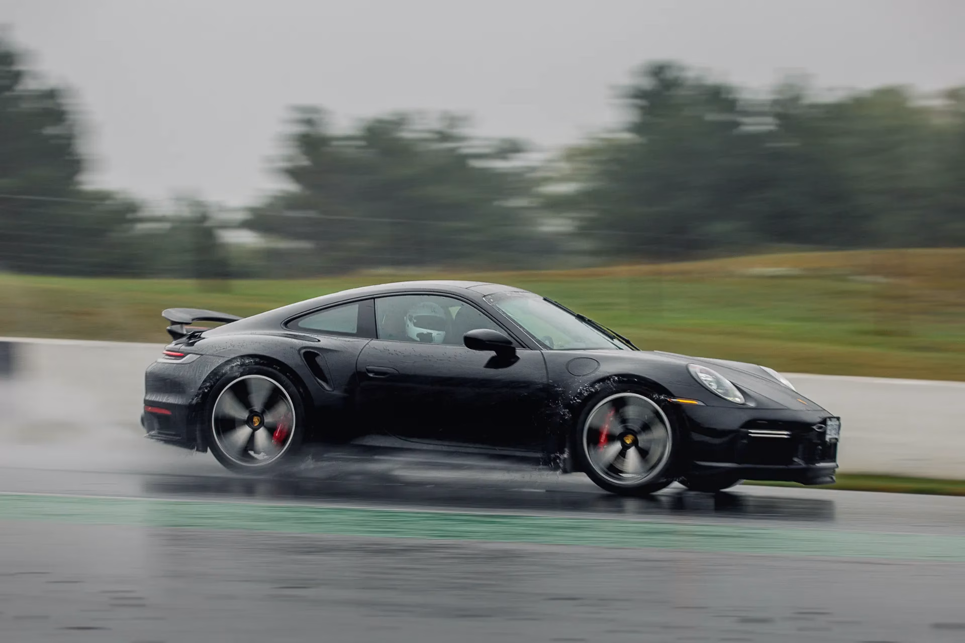 A black Porsche 911 Turbo S at speed on a wet track