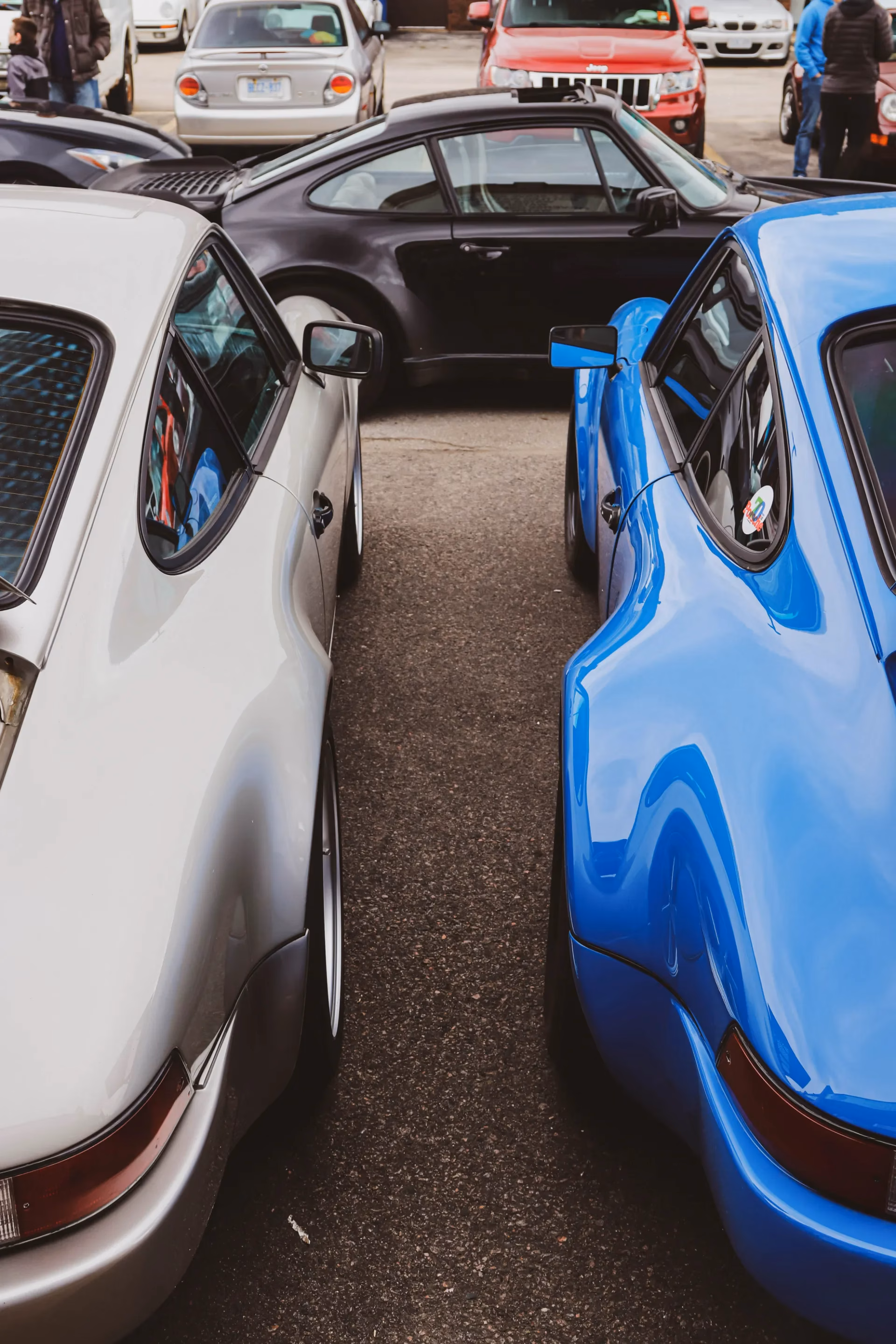 A silver and a blue classic air-cooled Porsche 911 parked side by side at a meet