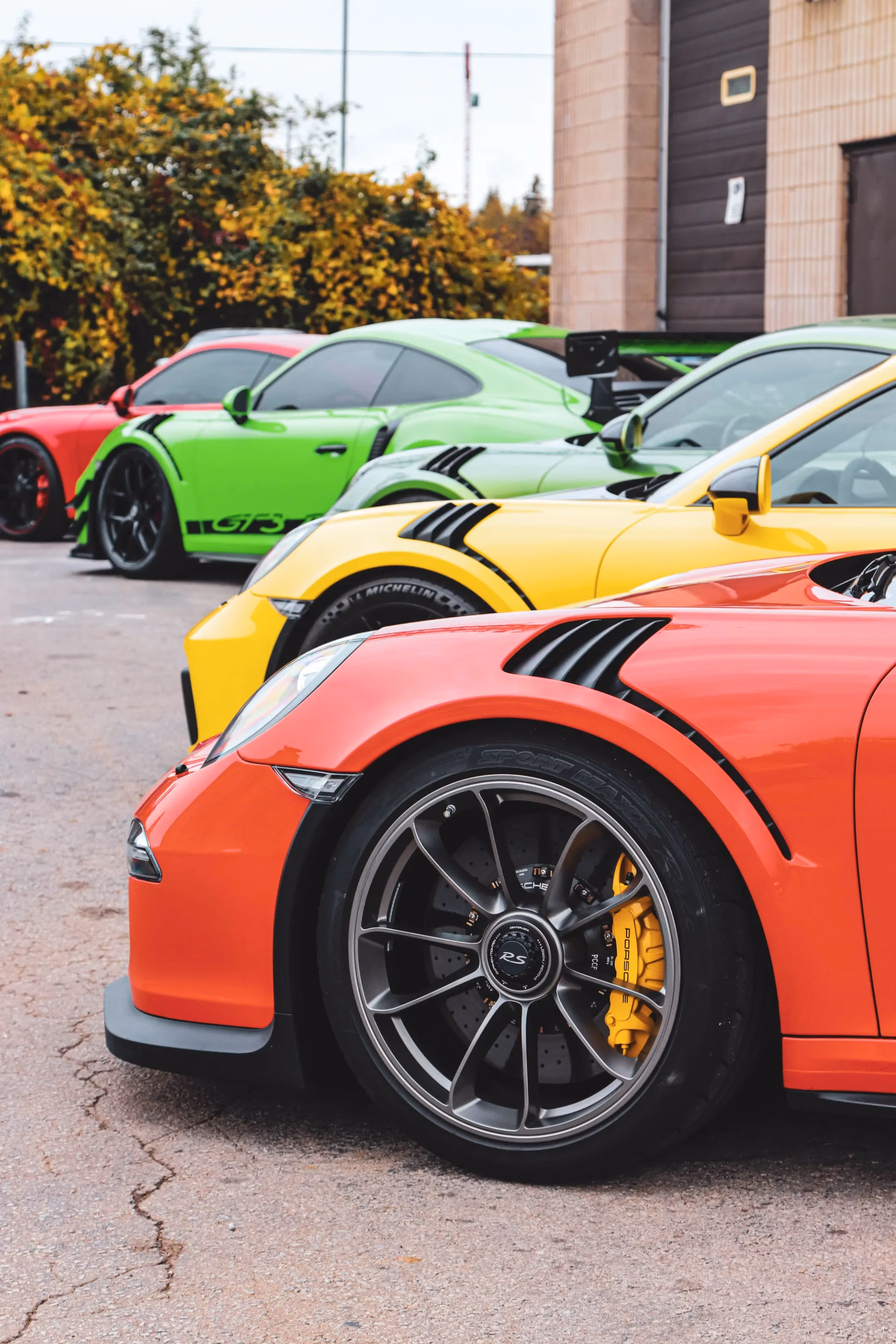 The front wheels of orange, yellow and green Porsche 911 GT3 RSs lined up at a meet
