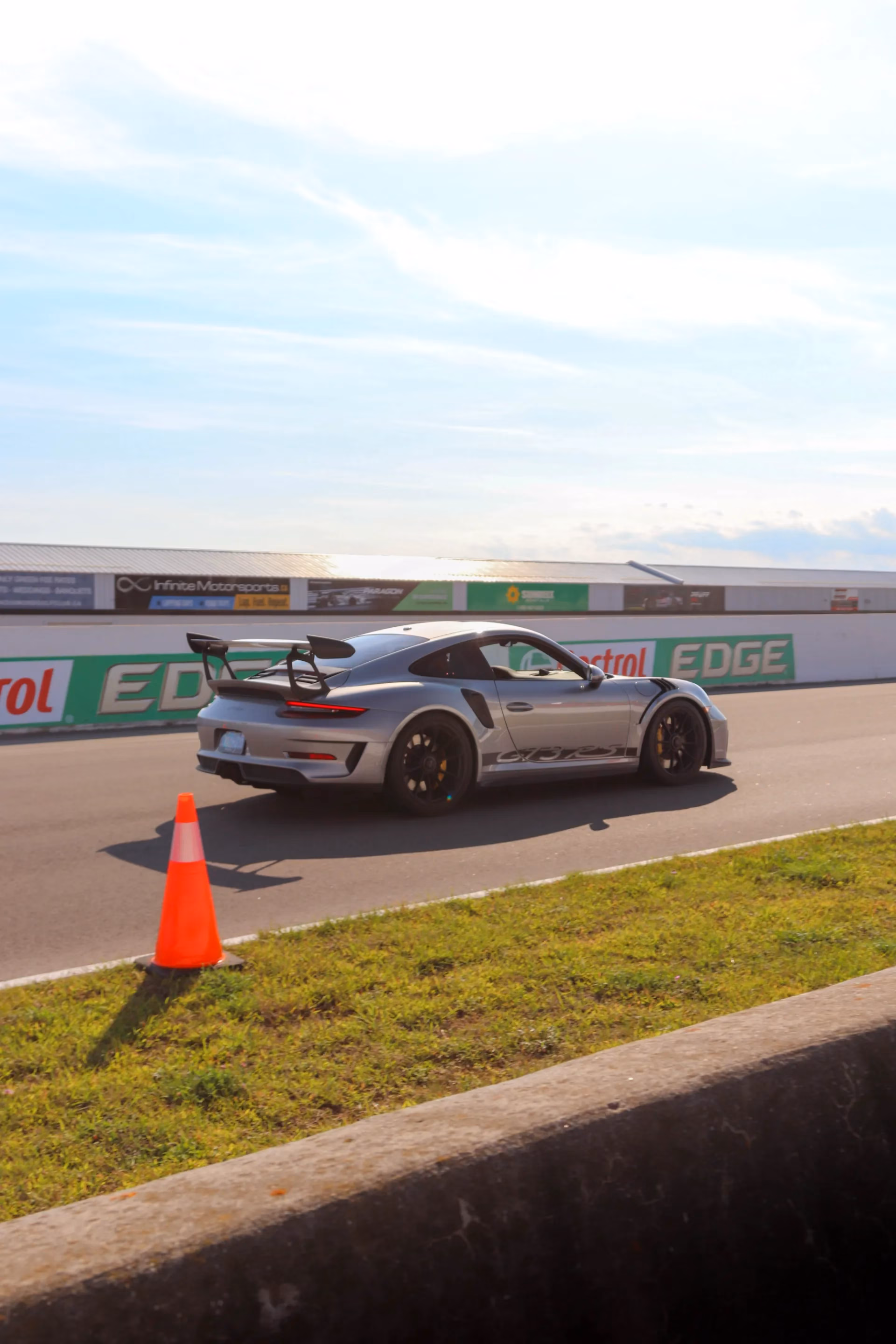 A silver Porsche 911 GT3 RS on track past trackside barriers