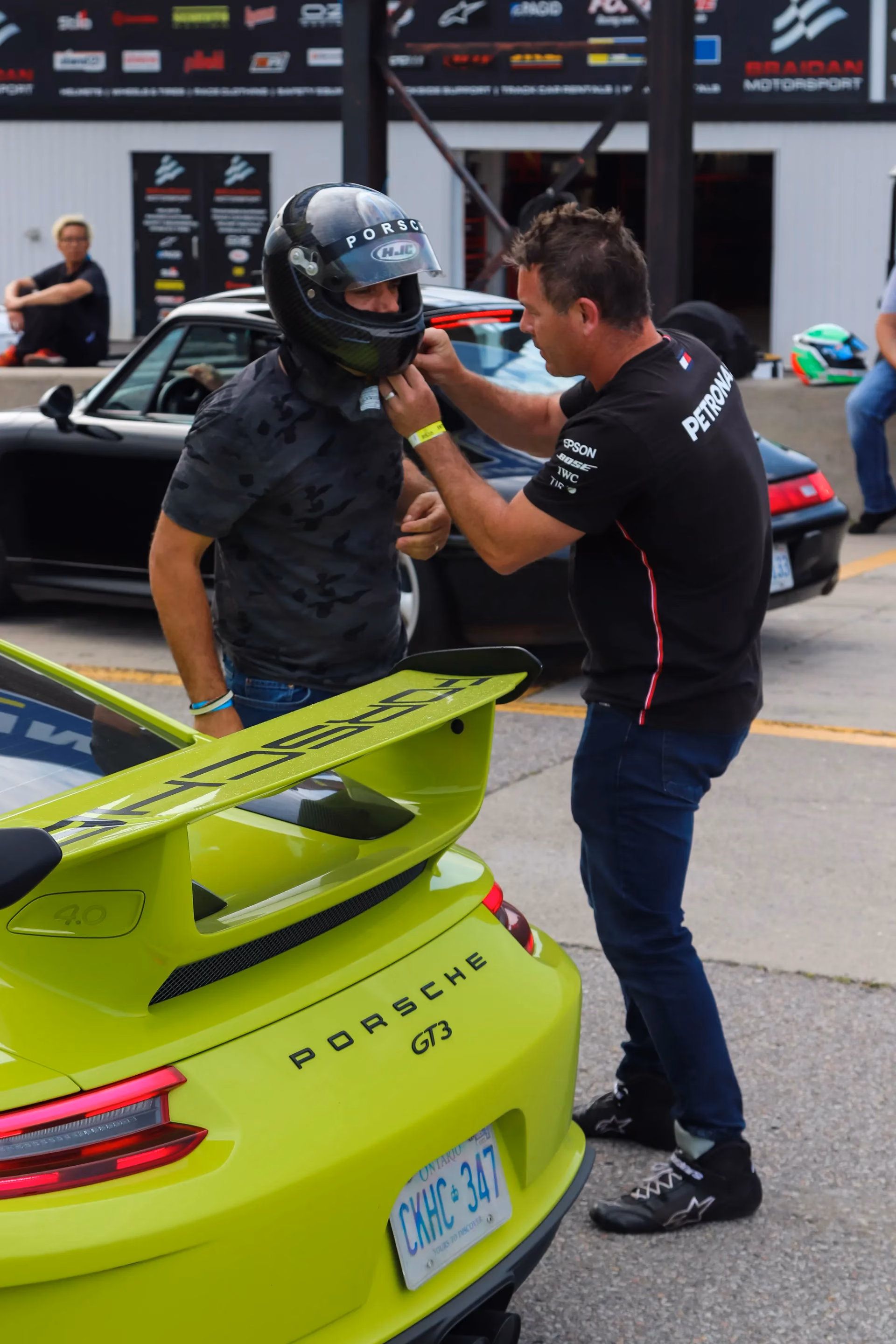 A driver being helped with his helmet beside a lime green Porsche 911 GT3 in the paddock