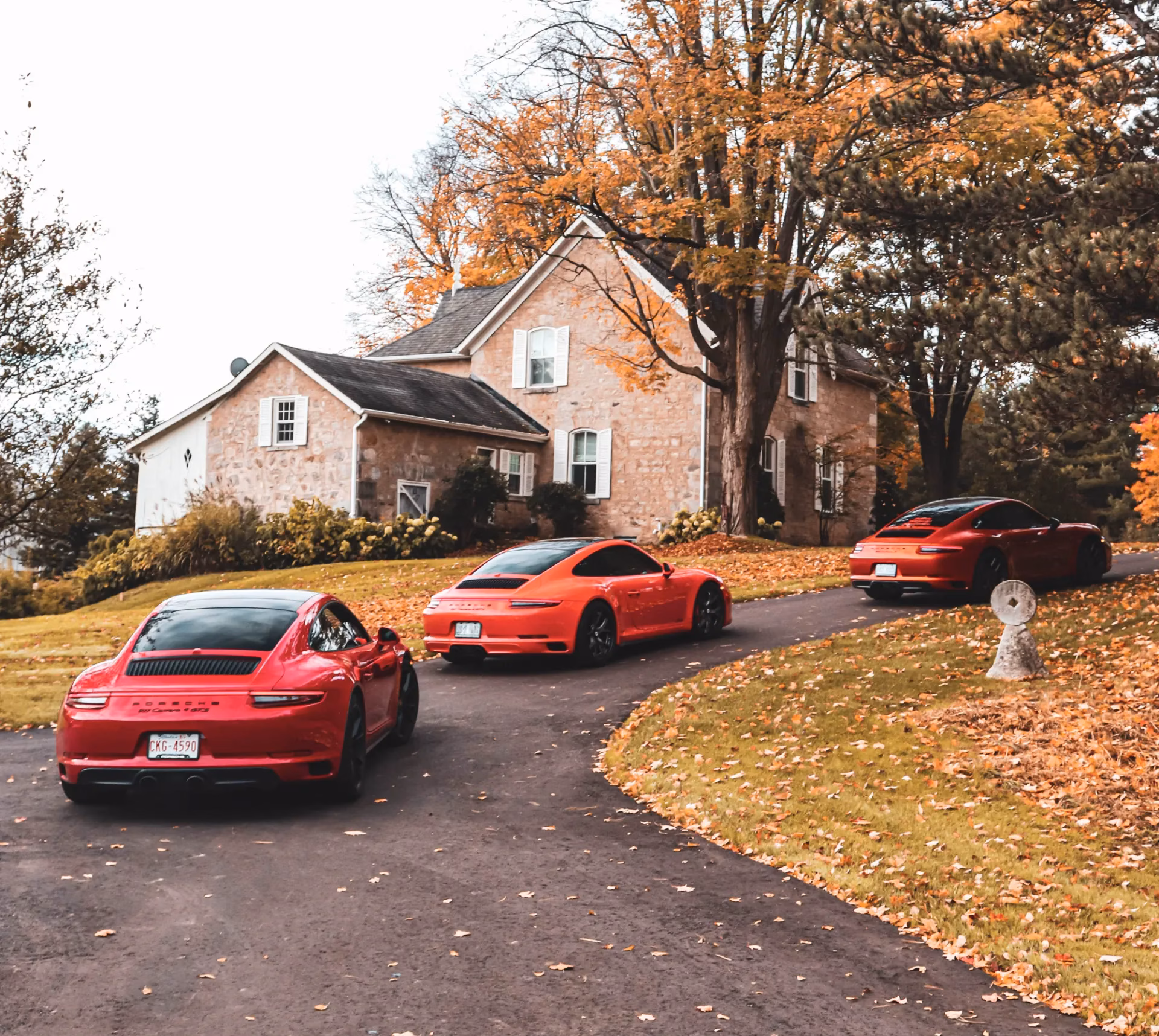 Three red Porsche 911s on the driveway of a stone farmhouse in autumn