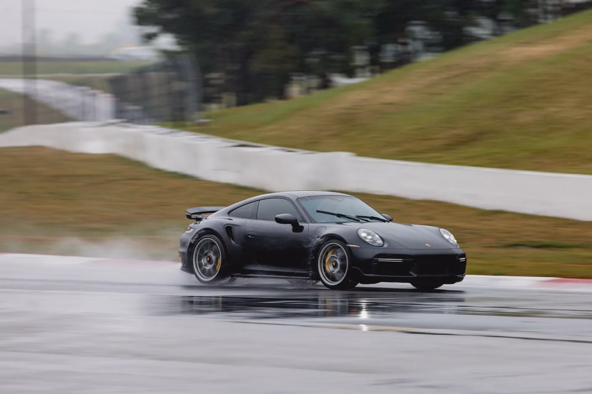 A black Porsche 911 Turbo S on a wet track, spray rising from the tyres