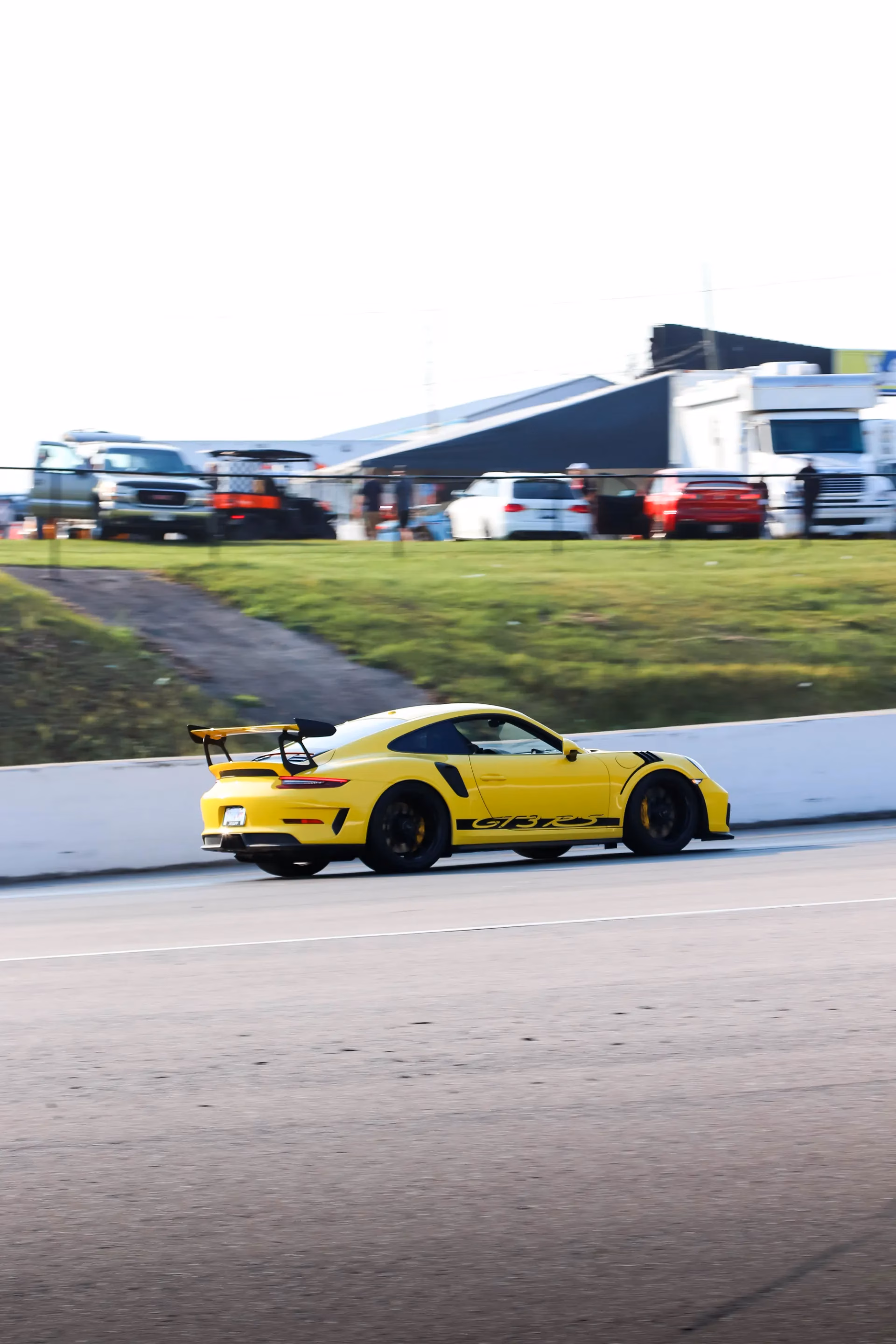 A yellow Porsche 911 GT3 RS on track, the paddock behind