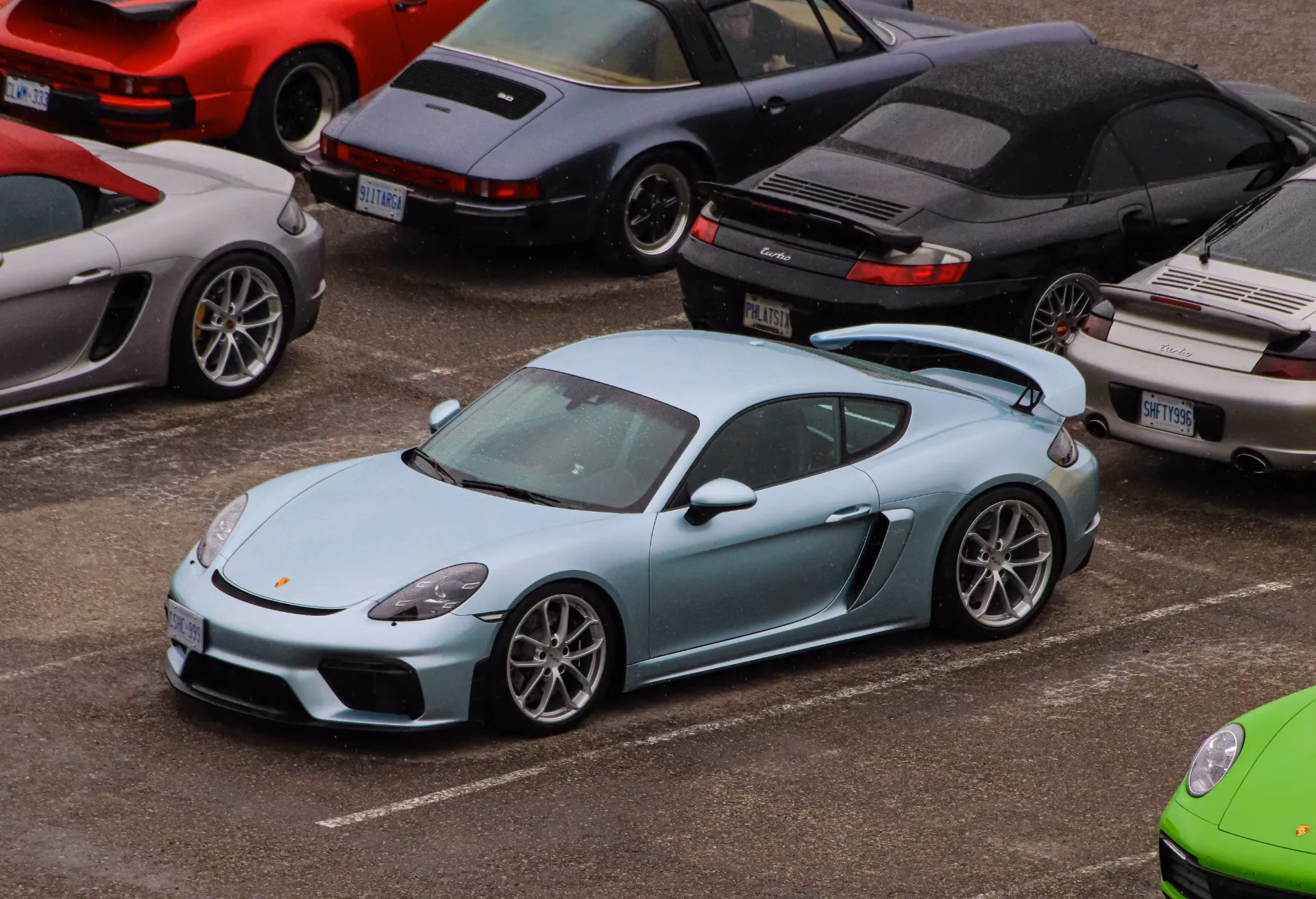 An ice blue Porsche Cayman parked among classic 911s, seen from above