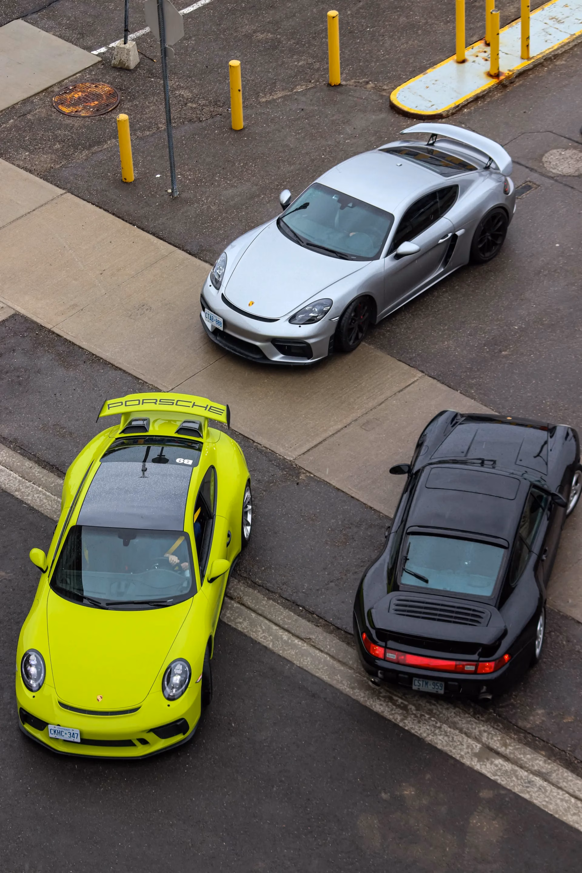 Overhead view of a silver Cayman, a lime green 911 and a black classic 911 parked at angles