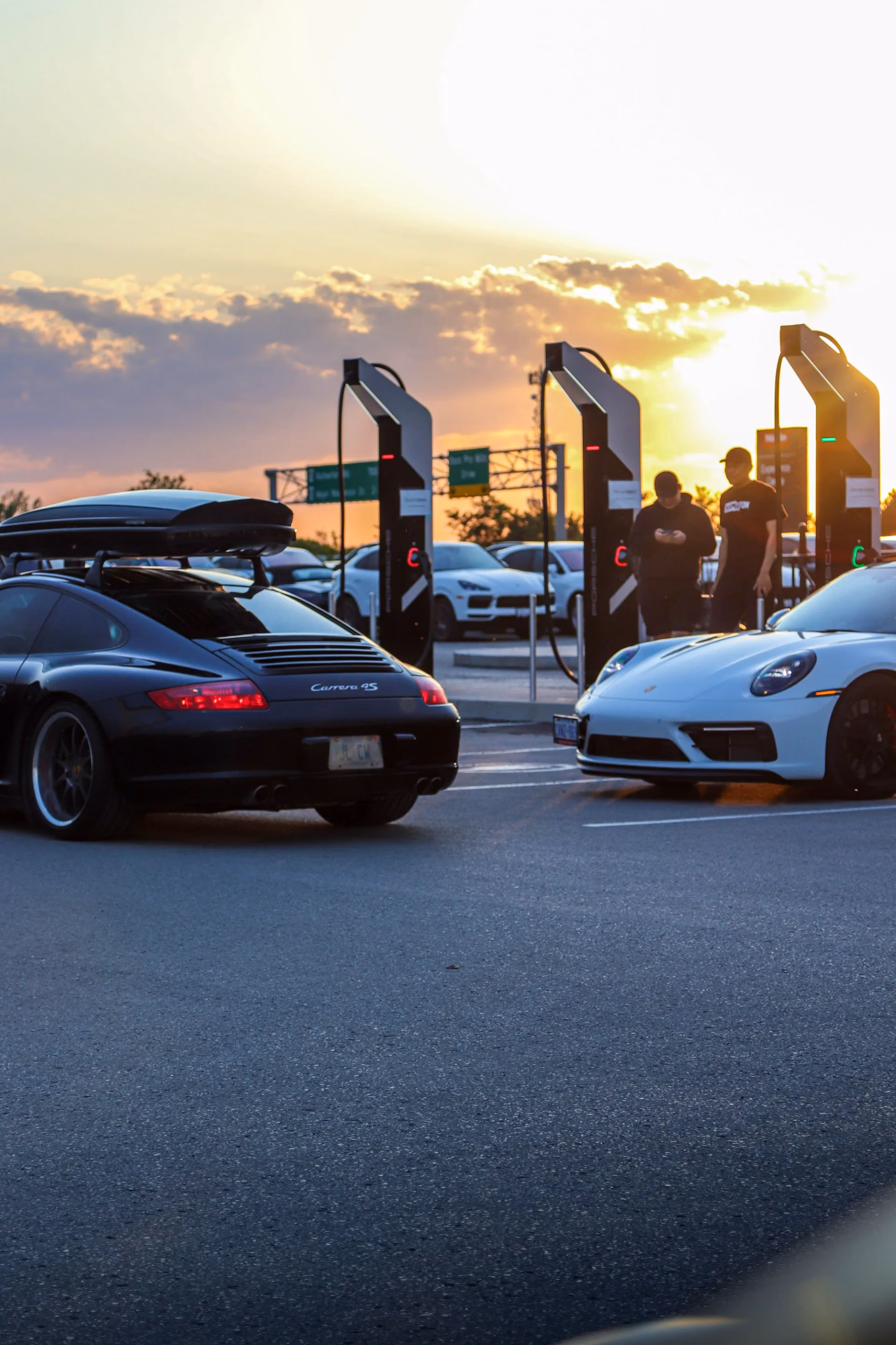 A black and a white Porsche parked at sunset beside event banners