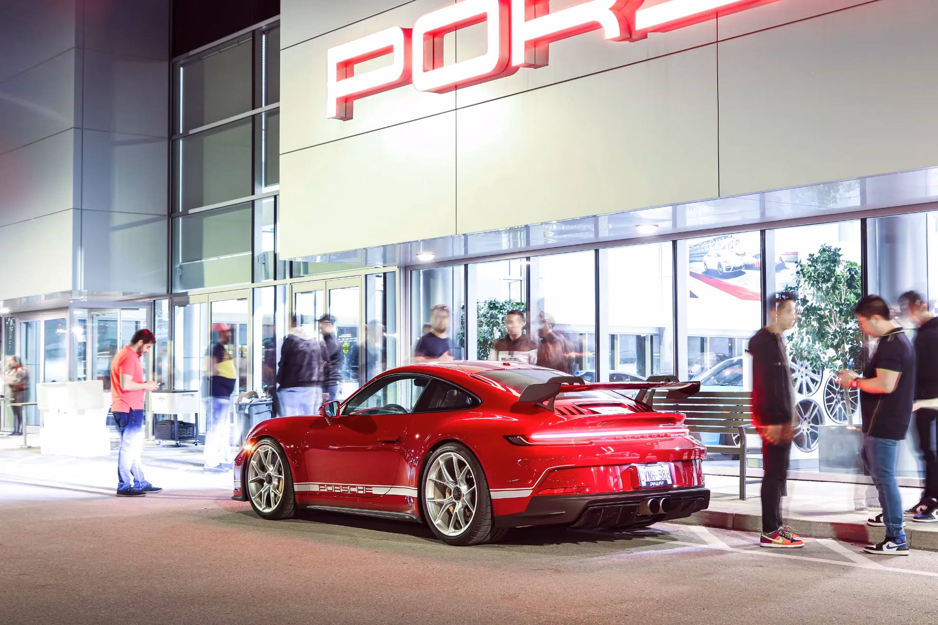 A red Porsche 911 parked at night outside a lit Porsche dealership
