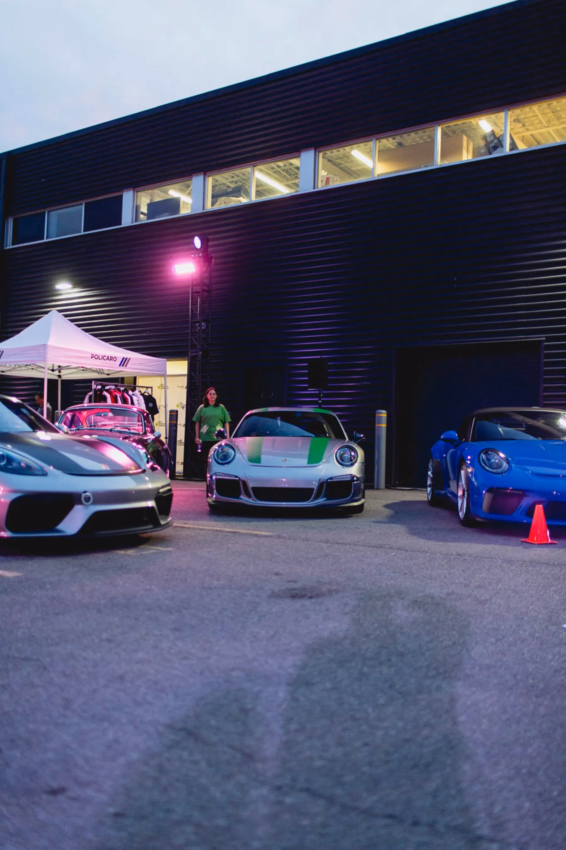 Porsches parked outside a dealership at dusk under coloured lighting