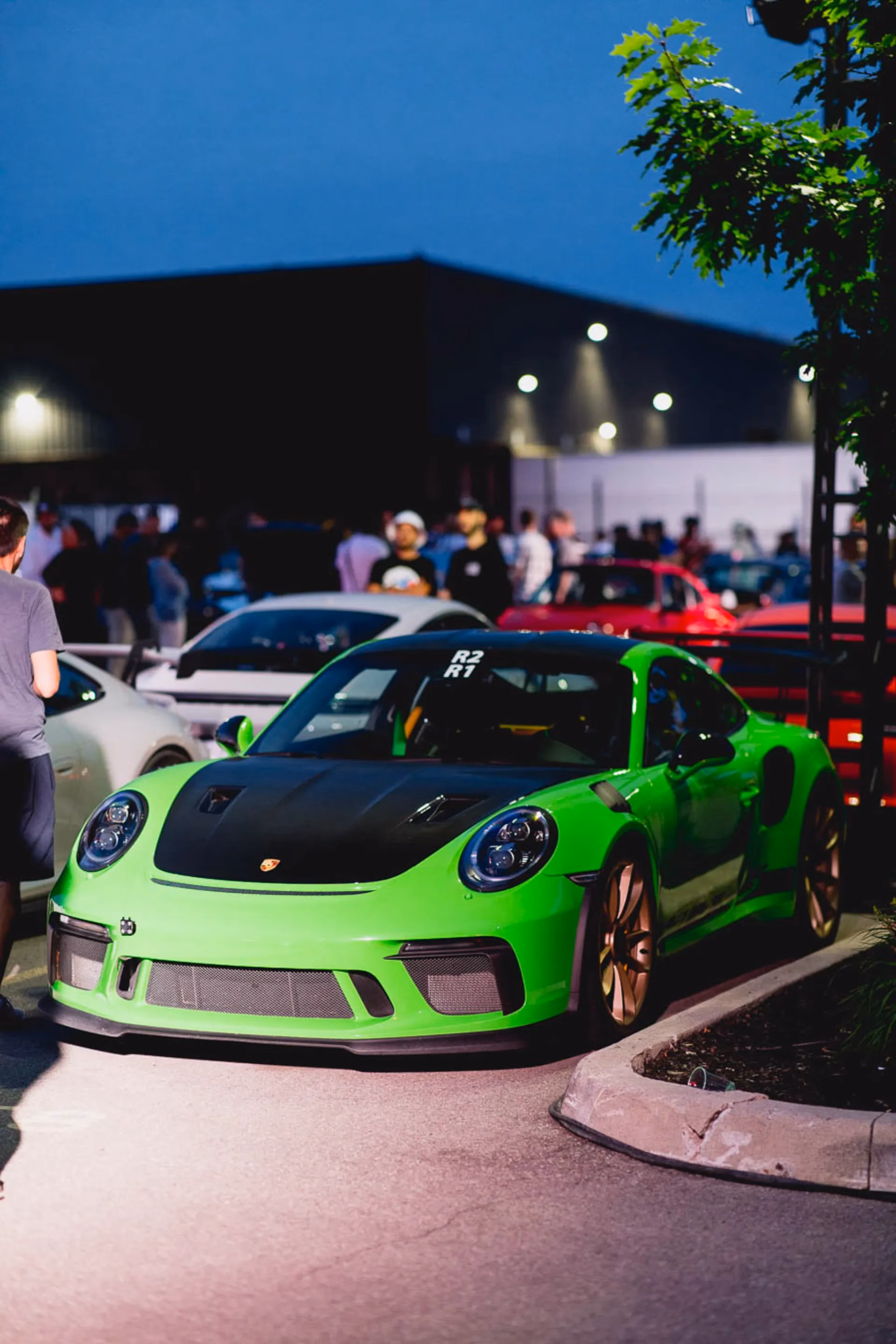 A lime green Porsche 911 with bronze wheels at an evening meet, members gathered behind