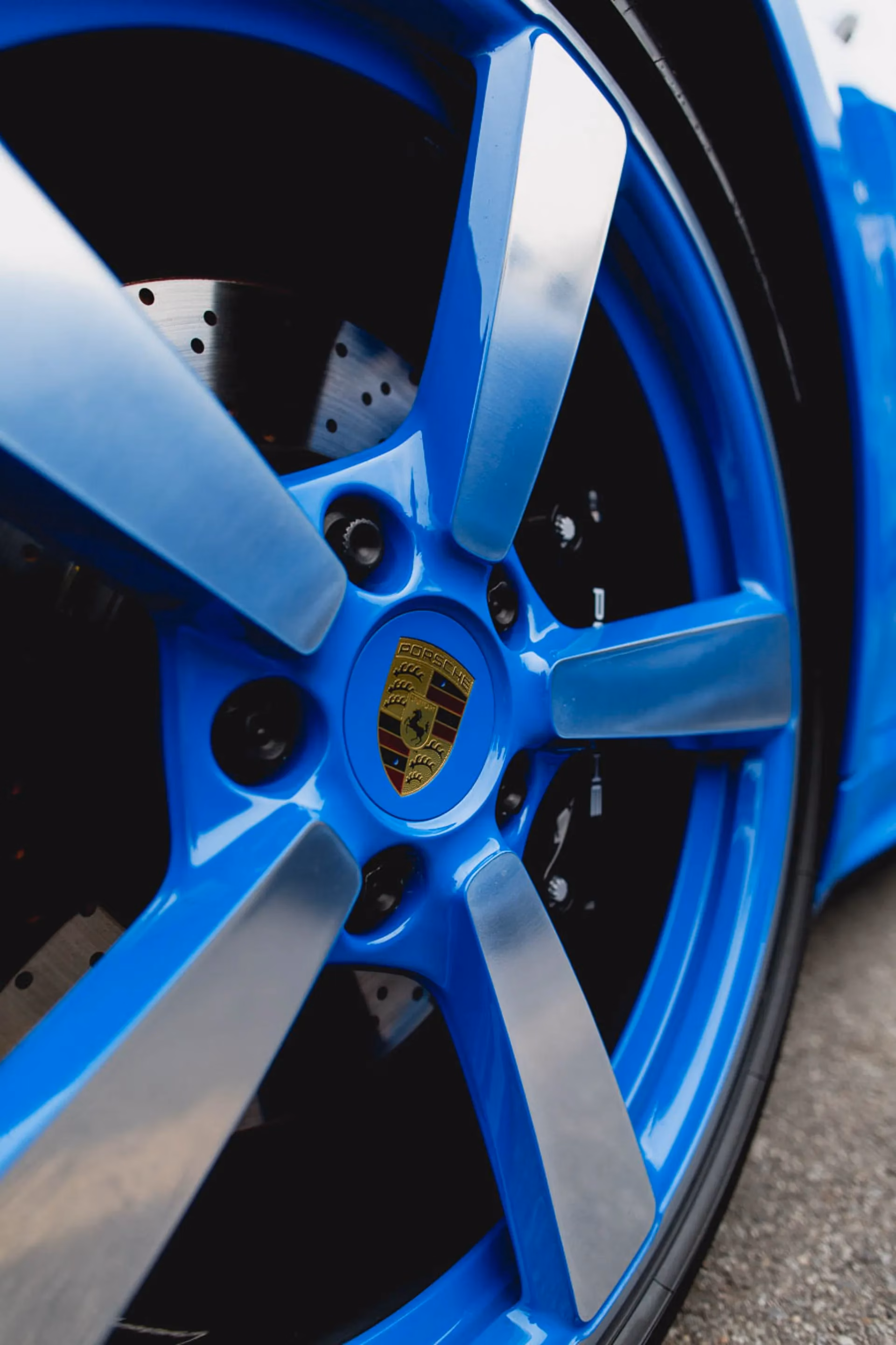 Close-up of a blue Porsche wheel and its crest centre cap, the brake disc visible behind the spokes