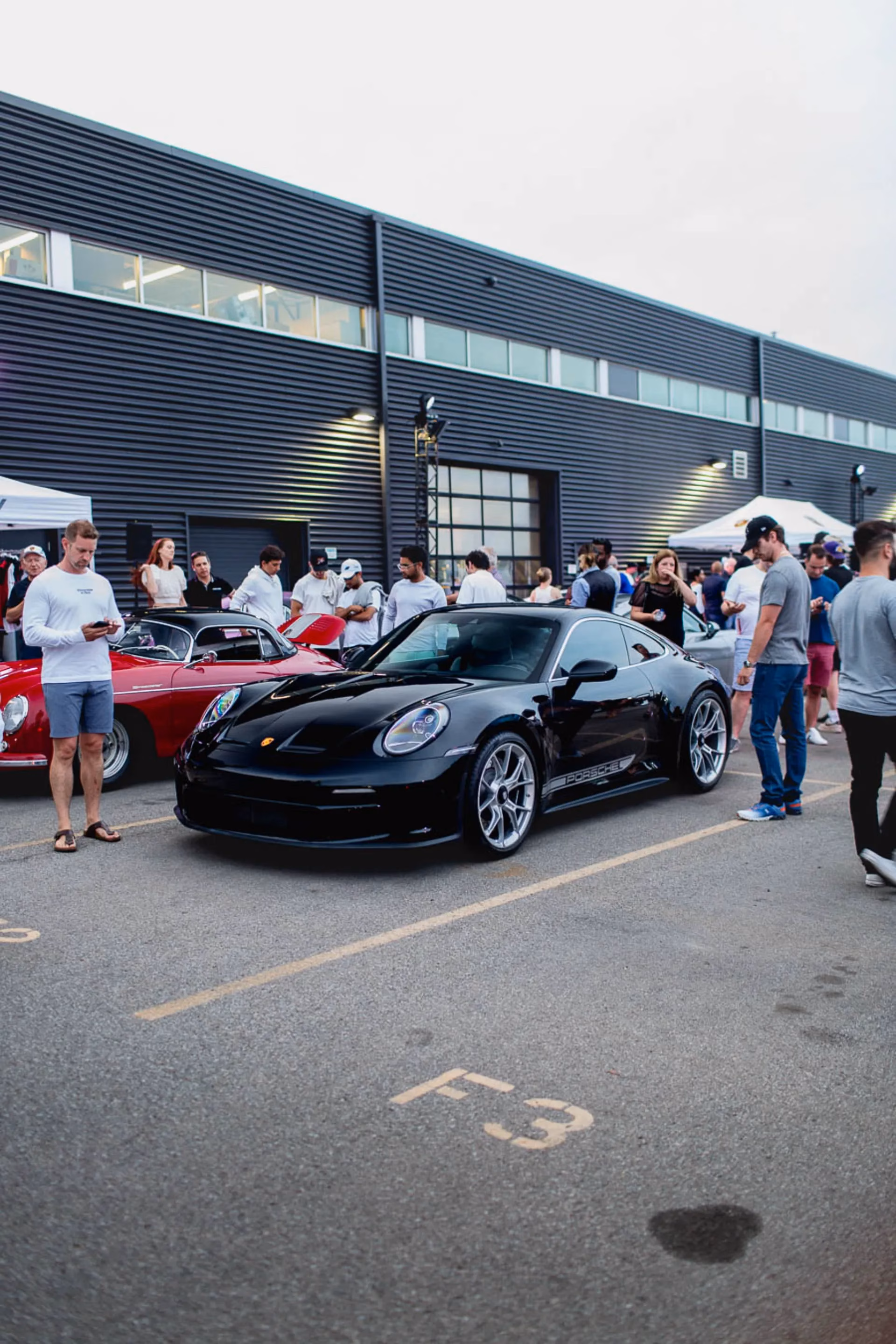 A black Porsche 911 parked at a busy evening meet, members gathered around it