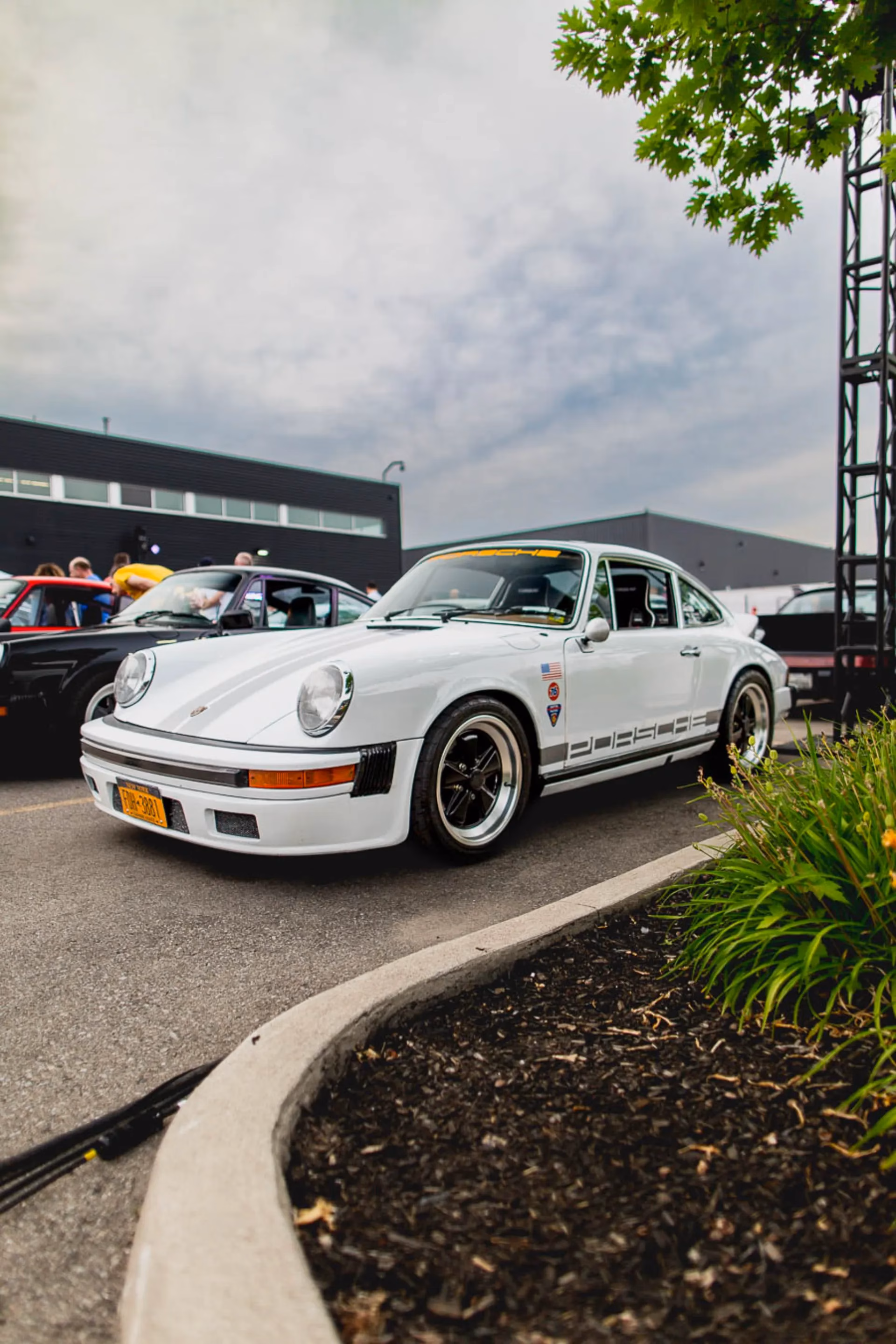 A white air-cooled Porsche 911 with black wheels and PORSCHE side script parked at a meet