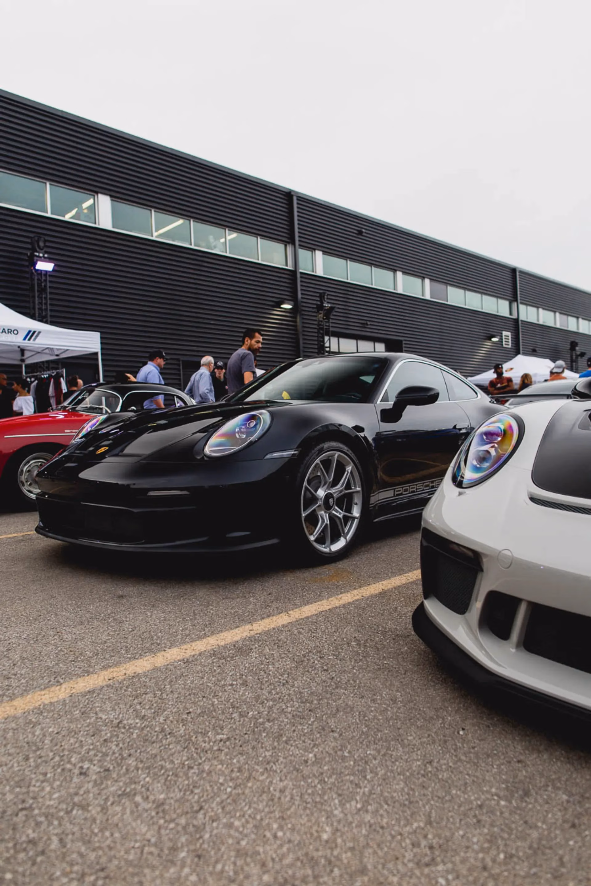 A black Porsche 911 parked between a red classic and a white 911 at a club meet