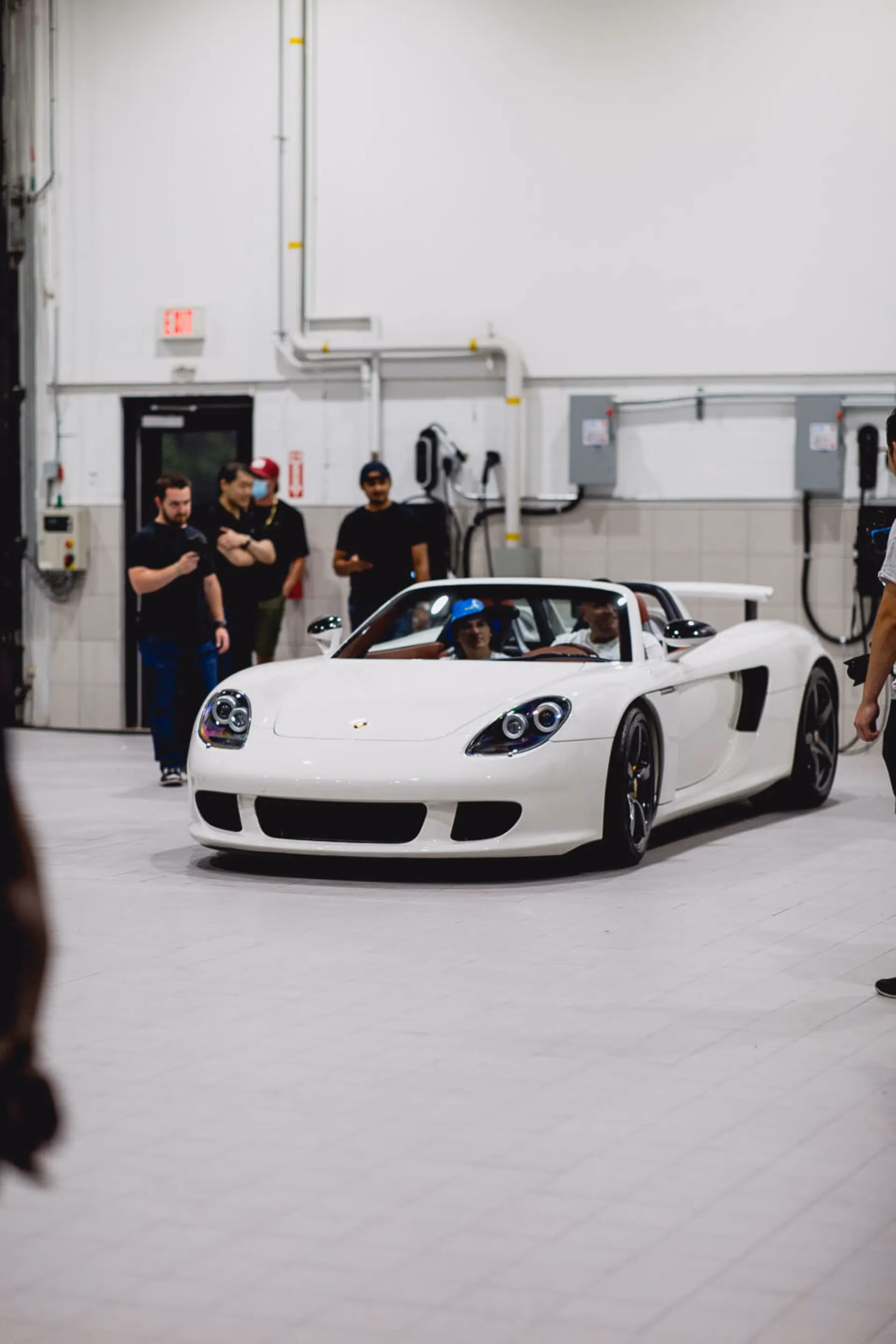 A white Porsche Carrera GT inside a service bay, members watching from the side