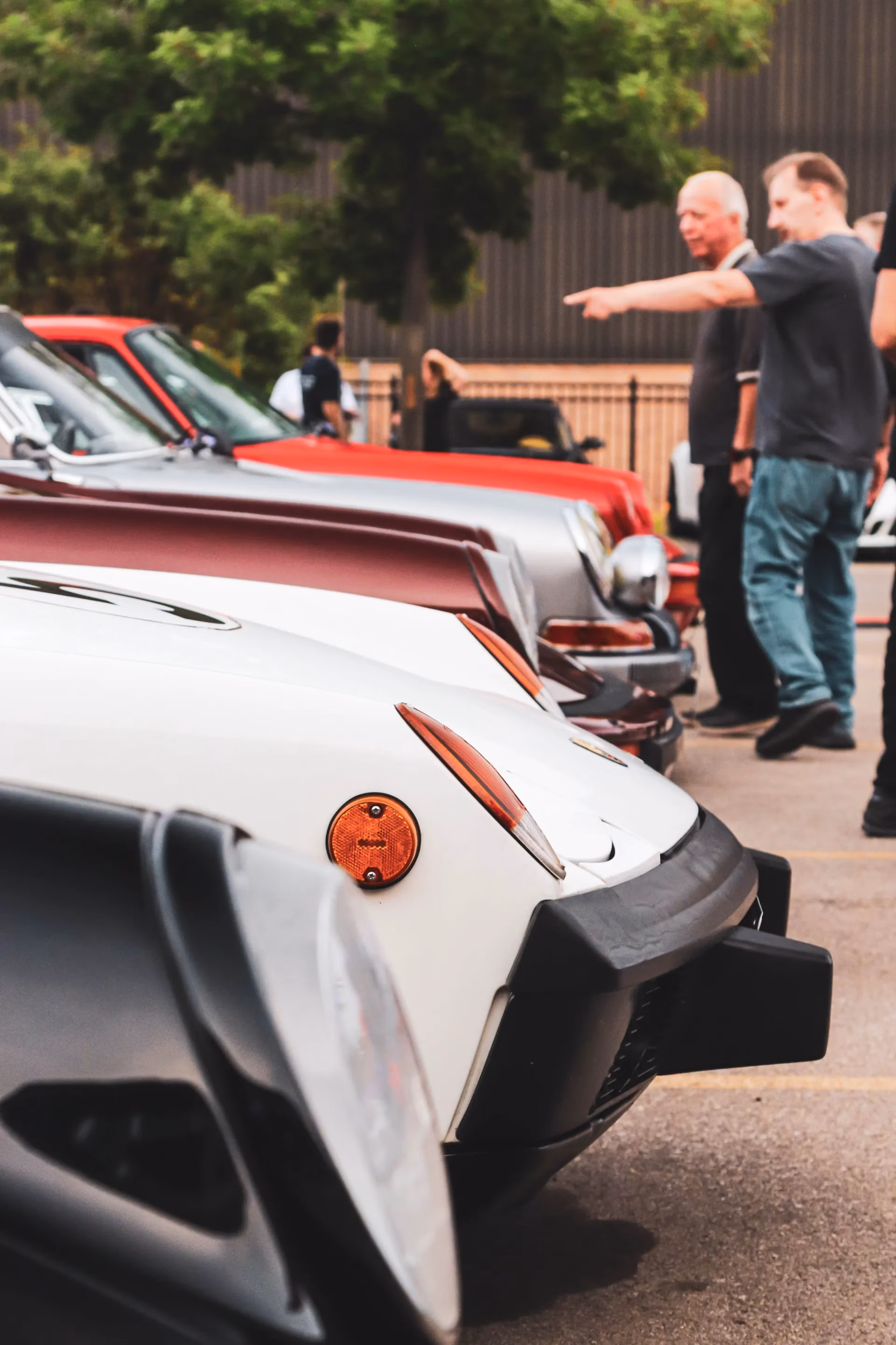 Front ends of classic Porsches lined up at a meet, members talking behind them