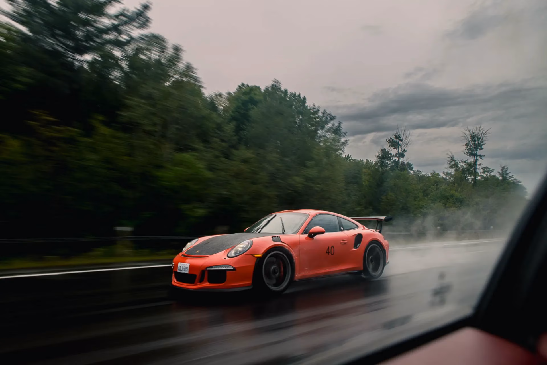 An orange Porsche 911 carrying race number 40 on a wet road, spray rising behind it