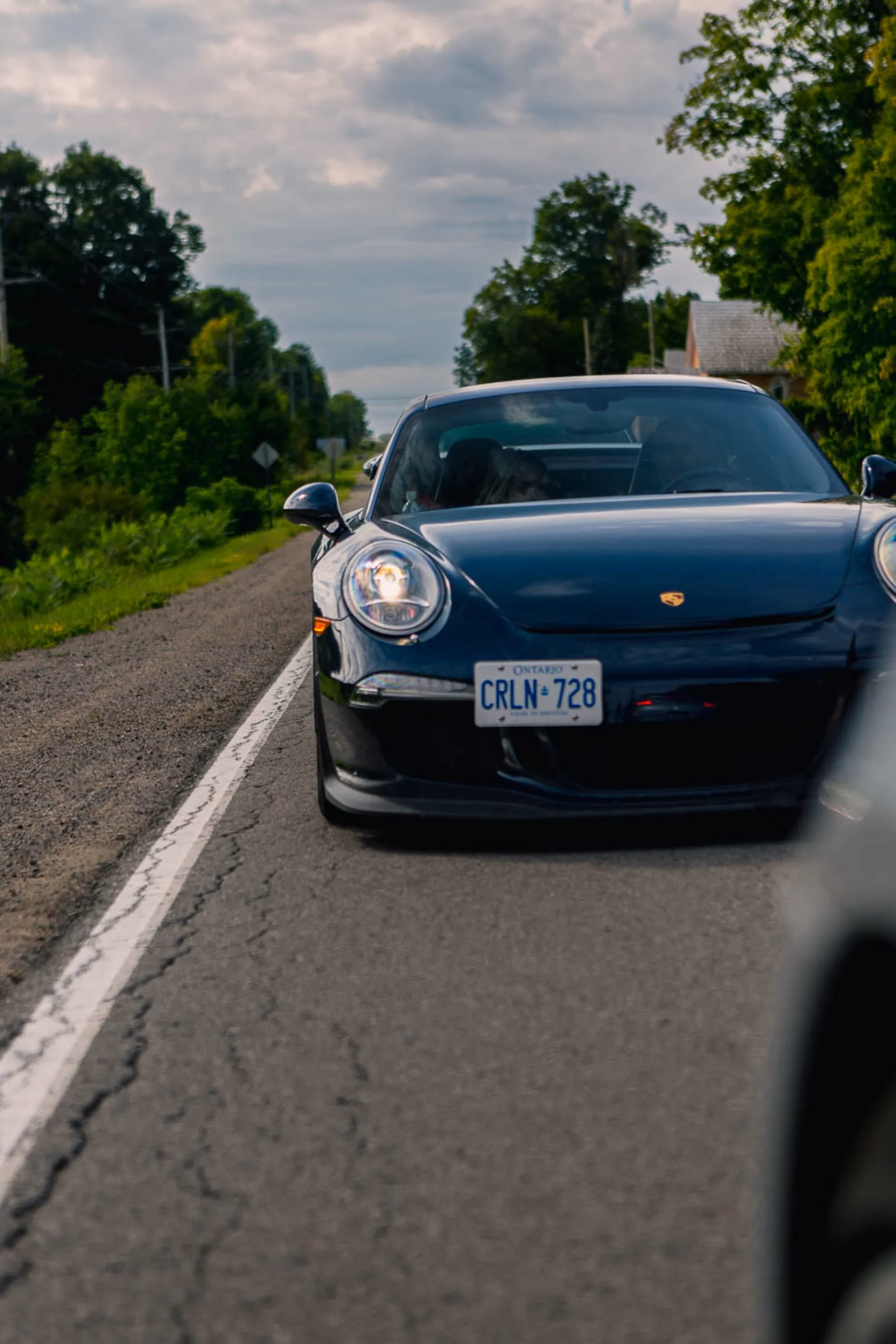 A dark blue Porsche 911 driving toward the camera on a country road
