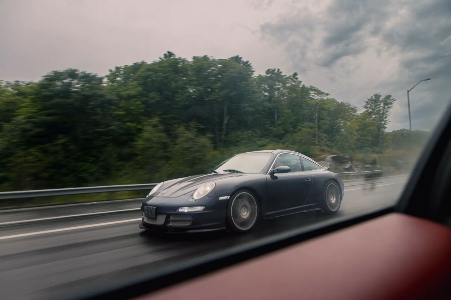 A dark blue Porsche 911 on a wet highway