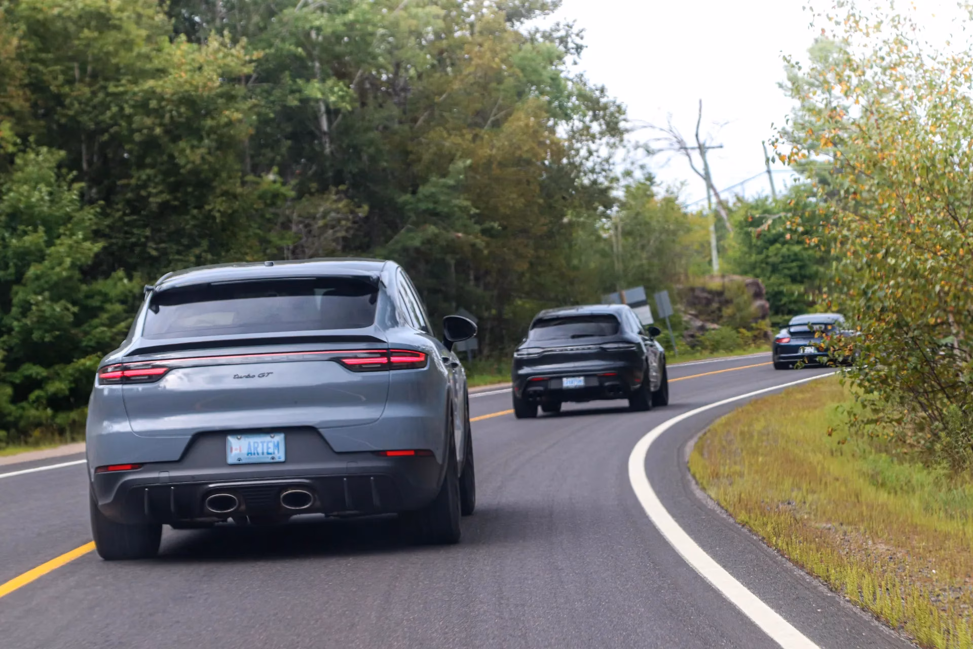 A grey Porsche Cayenne Coupe following other Porsches along a forest road