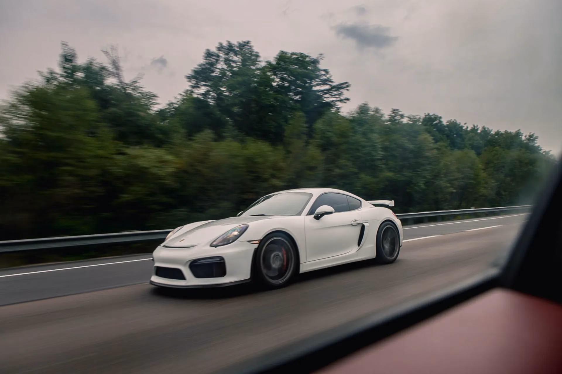 A white Porsche Cayman GT4 at speed on a country road