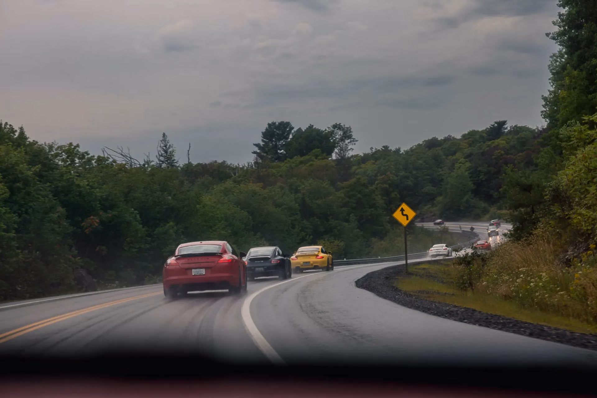 A convoy of Porsches on a wet winding road, seen through the windscreen of a following car