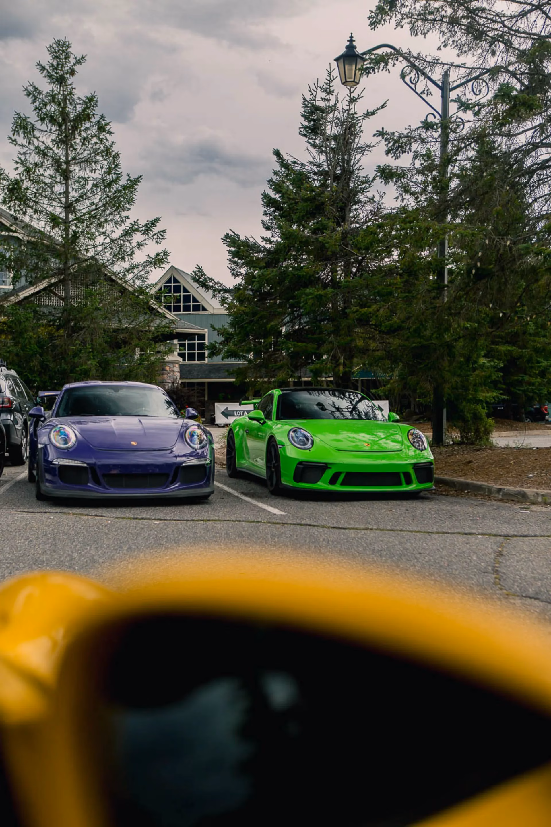 A purple and a lime green Porsche 911 parked side by side outside a lodge