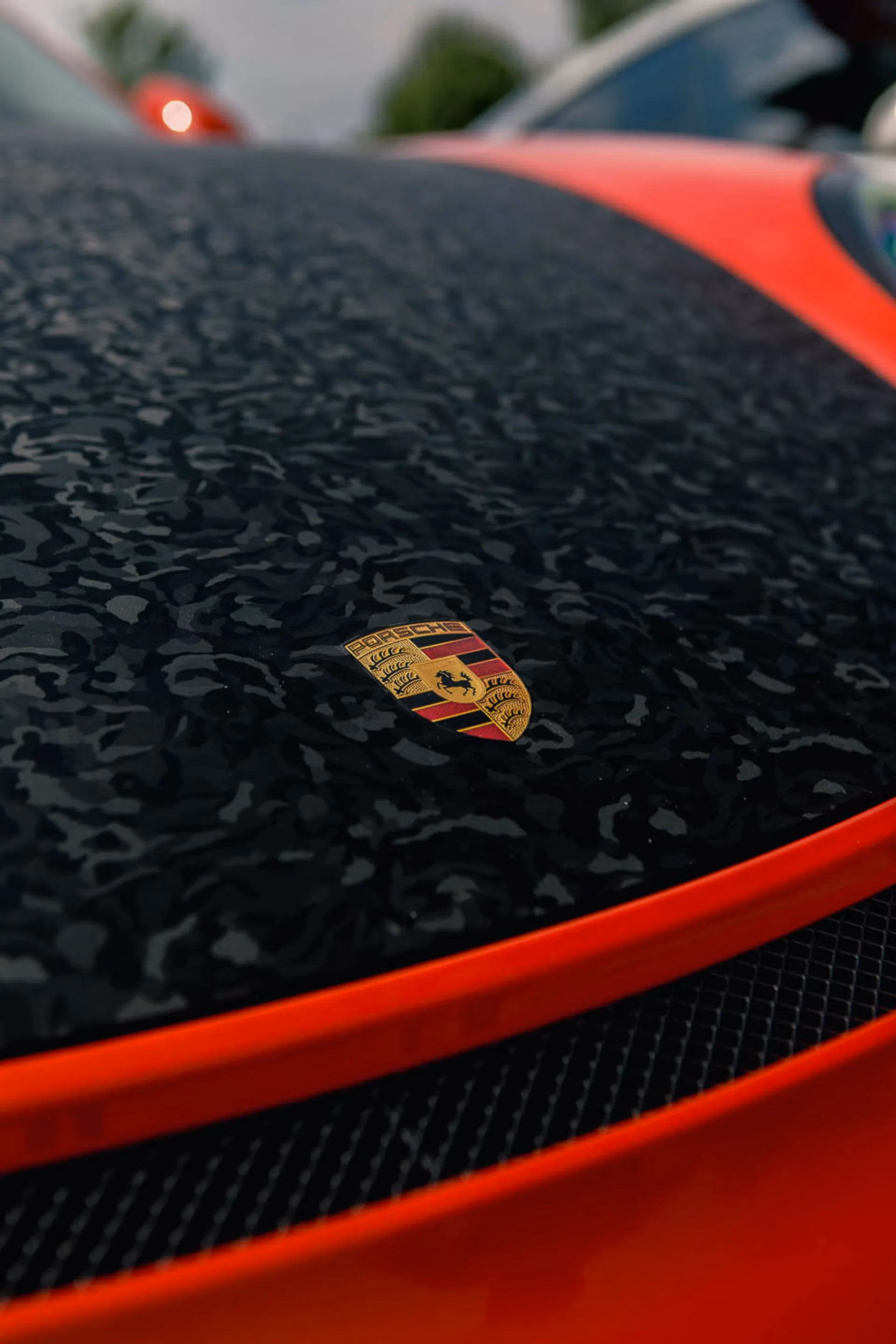 Close-up of the Porsche crest on the carbon fibre hood of a red car