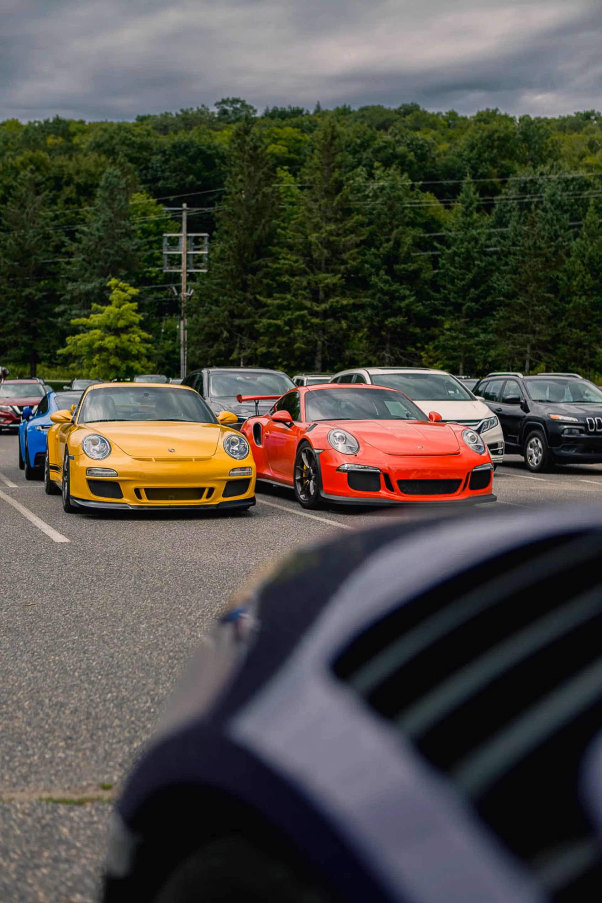 A yellow and a red Porsche 911 GT3 RS parked nose-out with forest behind