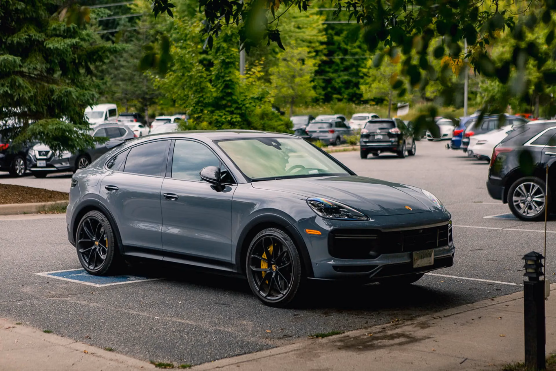 A grey Porsche Cayenne Coupe parked in a tree-lined lot