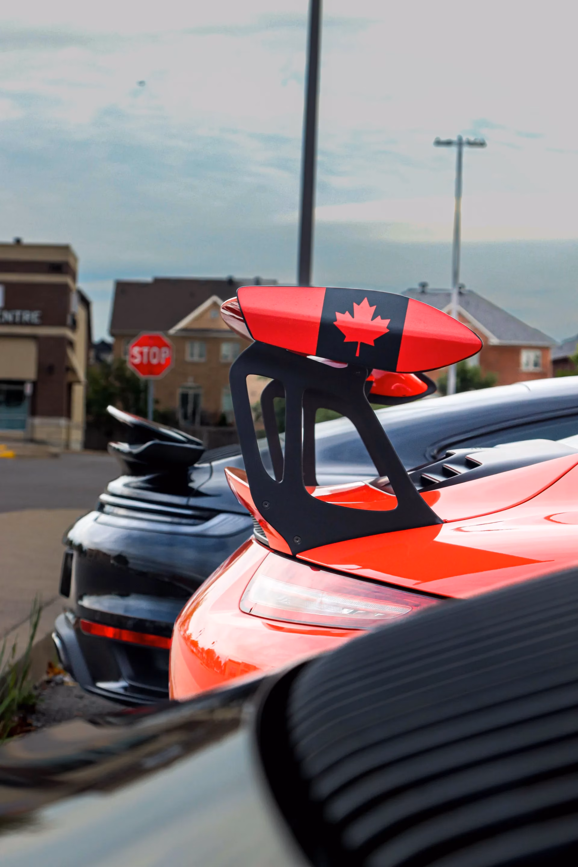 A rear wing painted with the Canadian flag on a red Porsche at a roadside stop
