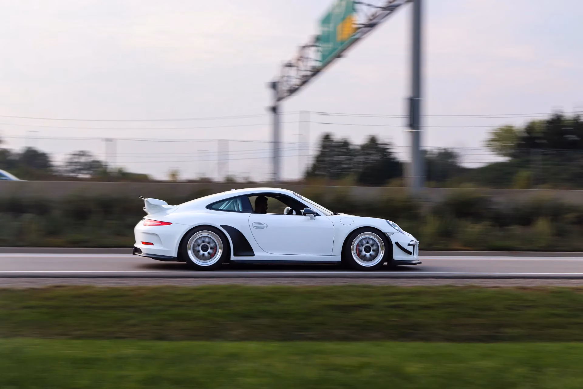 A white Porsche 911 at speed on the highway, panned to blur the background