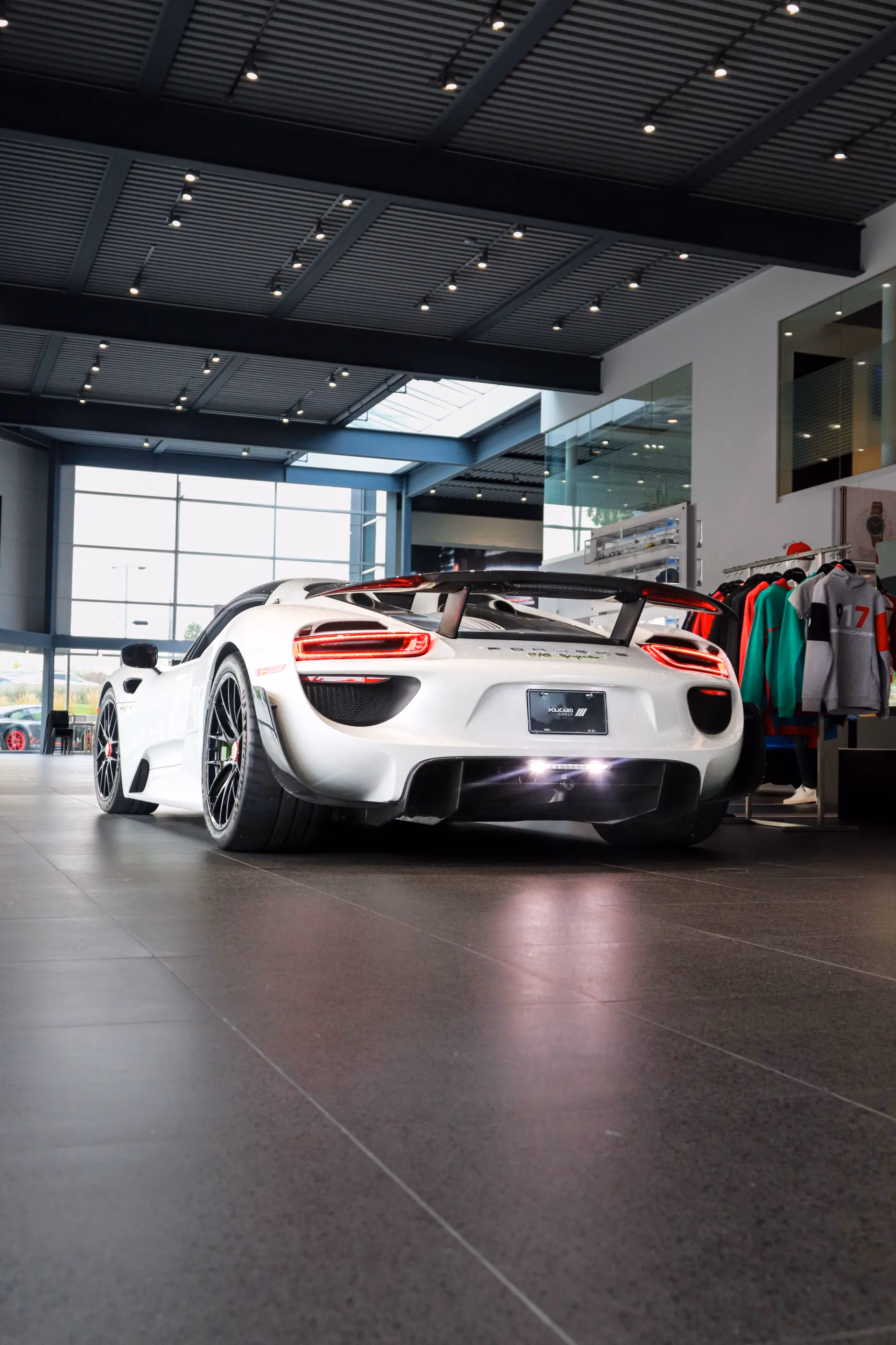 Rear view of a white Porsche 918 Spyder in a showroom, its top-exit exhausts lit