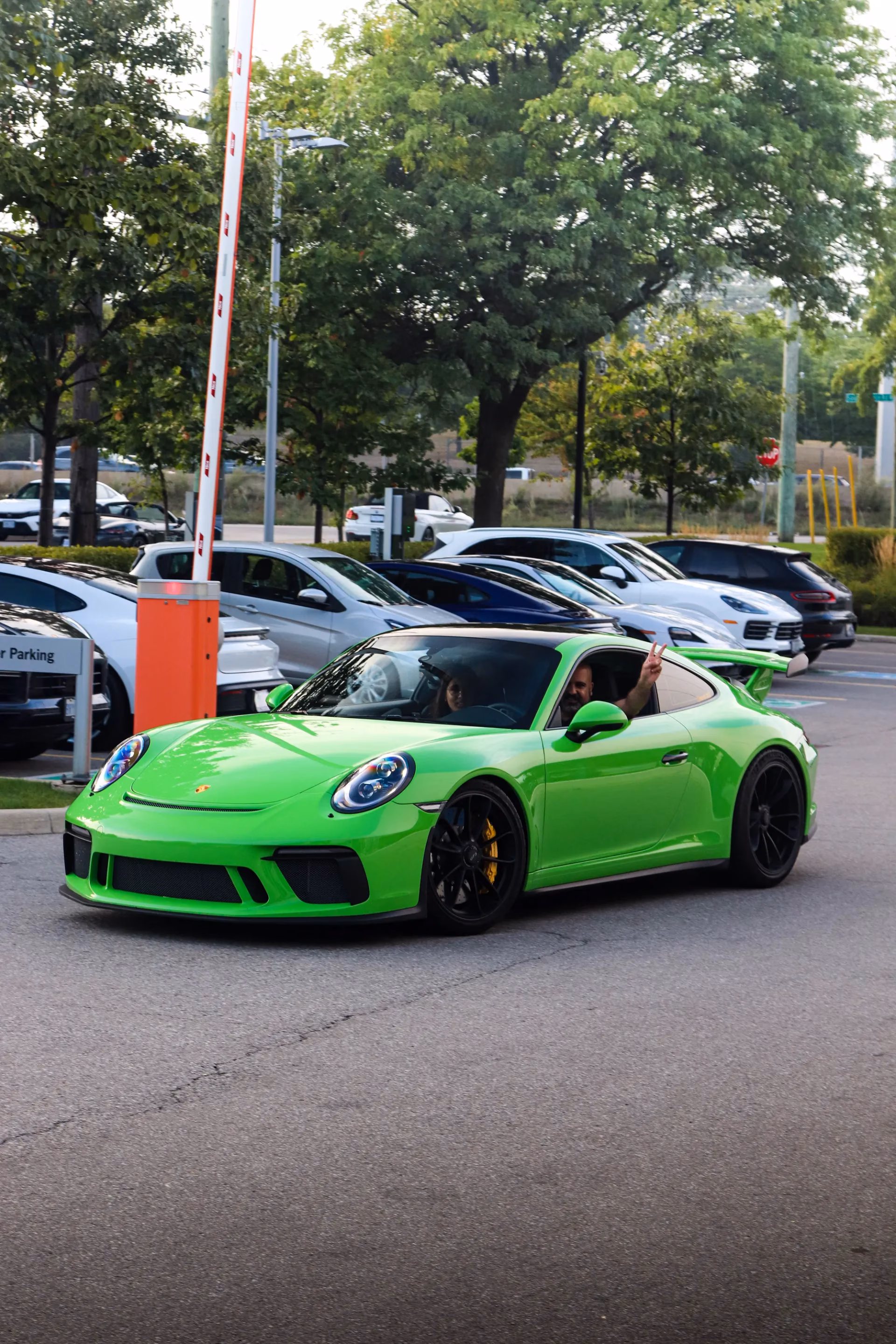 A lime green Porsche 911 pulling out of a parking lot, the driver waving