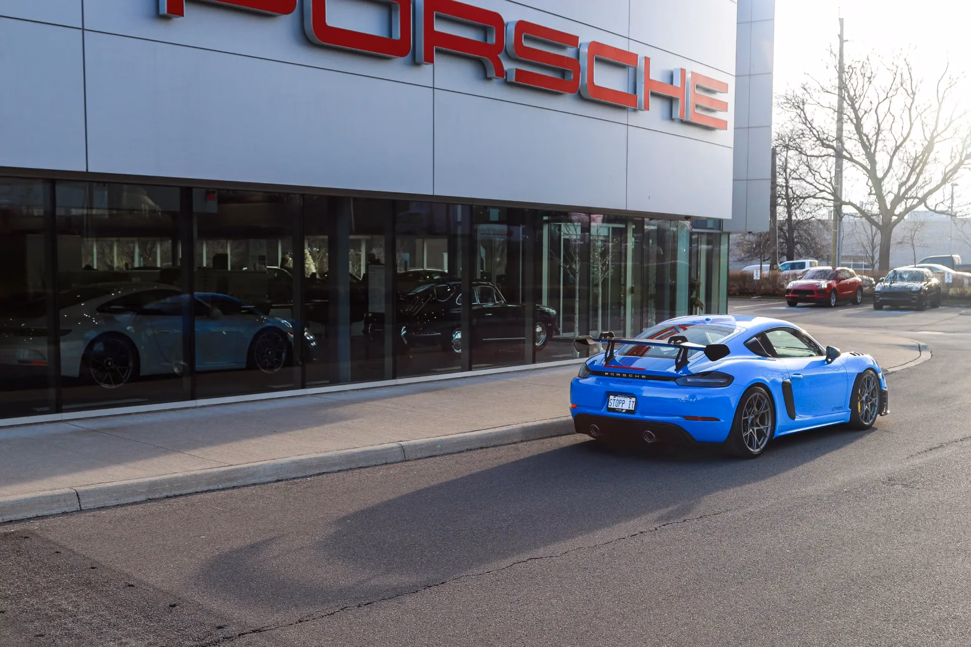A blue Porsche Cayman GT4 RS parked outside a Porsche dealership