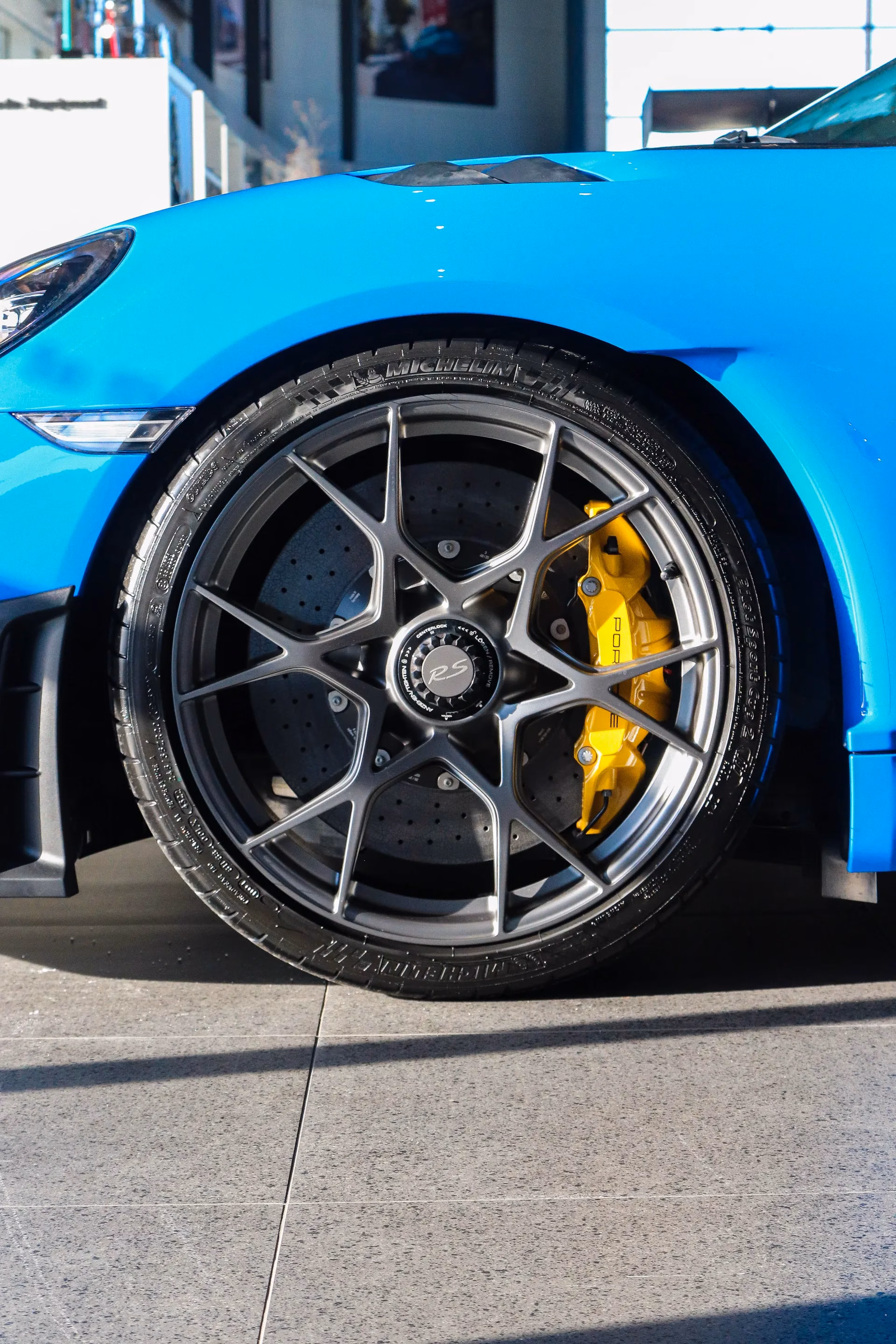 Close-up of a blue Porsche Cayman's wheel and yellow ceramic brake caliper