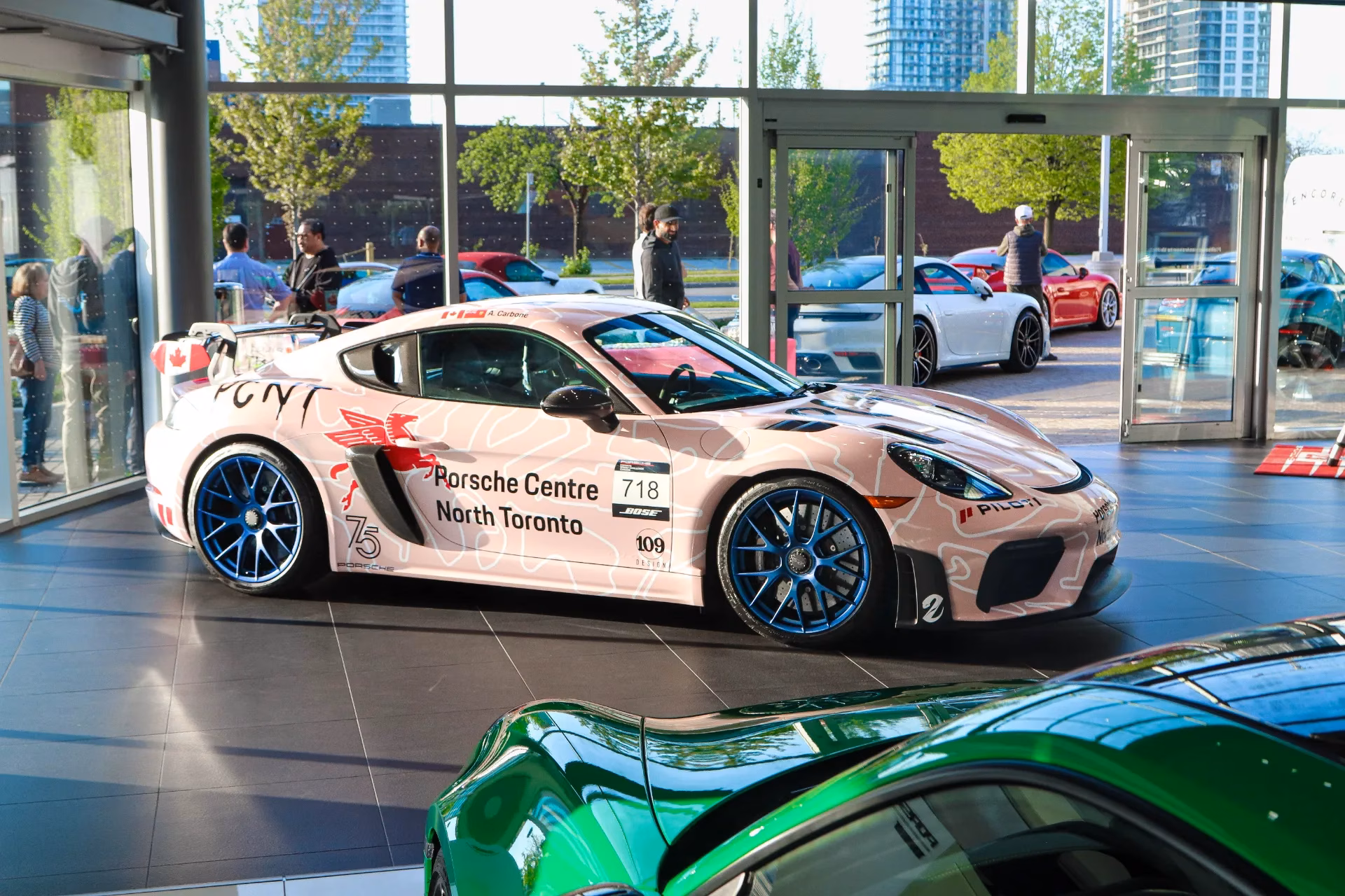 A Porsche Cayman in pink and white Porsche Centre North Toronto race livery inside a showroom