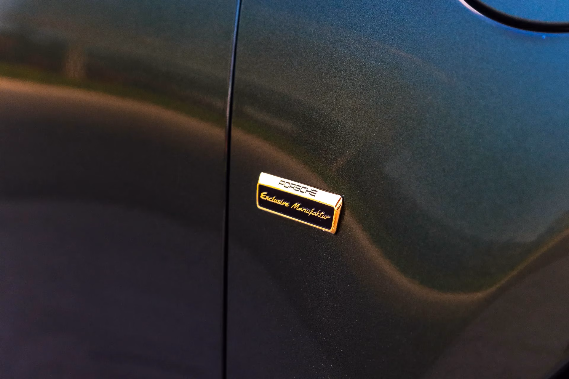 Close-up of a gold Porsche Exclusive Manufaktur badge on a dark green car
