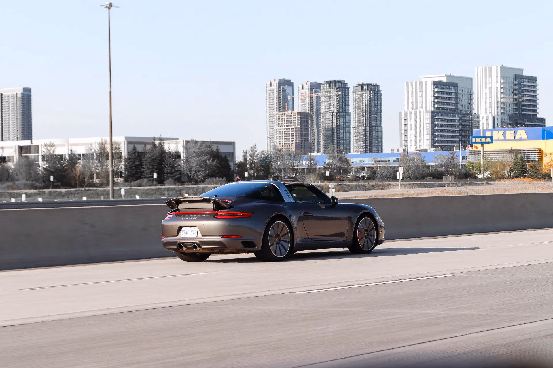A grey Porsche 911 Targa on the highway, condo towers and an IKEA store behind