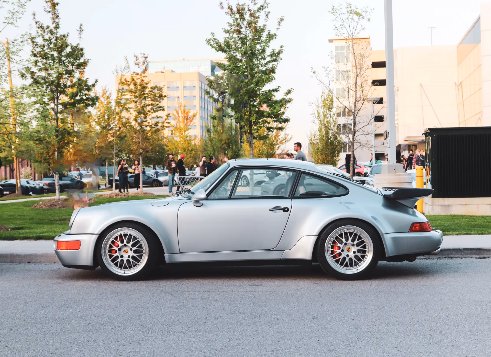 A silver classic Porsche 911 Turbo with a whale-tail spoiler parked in profile at a meet