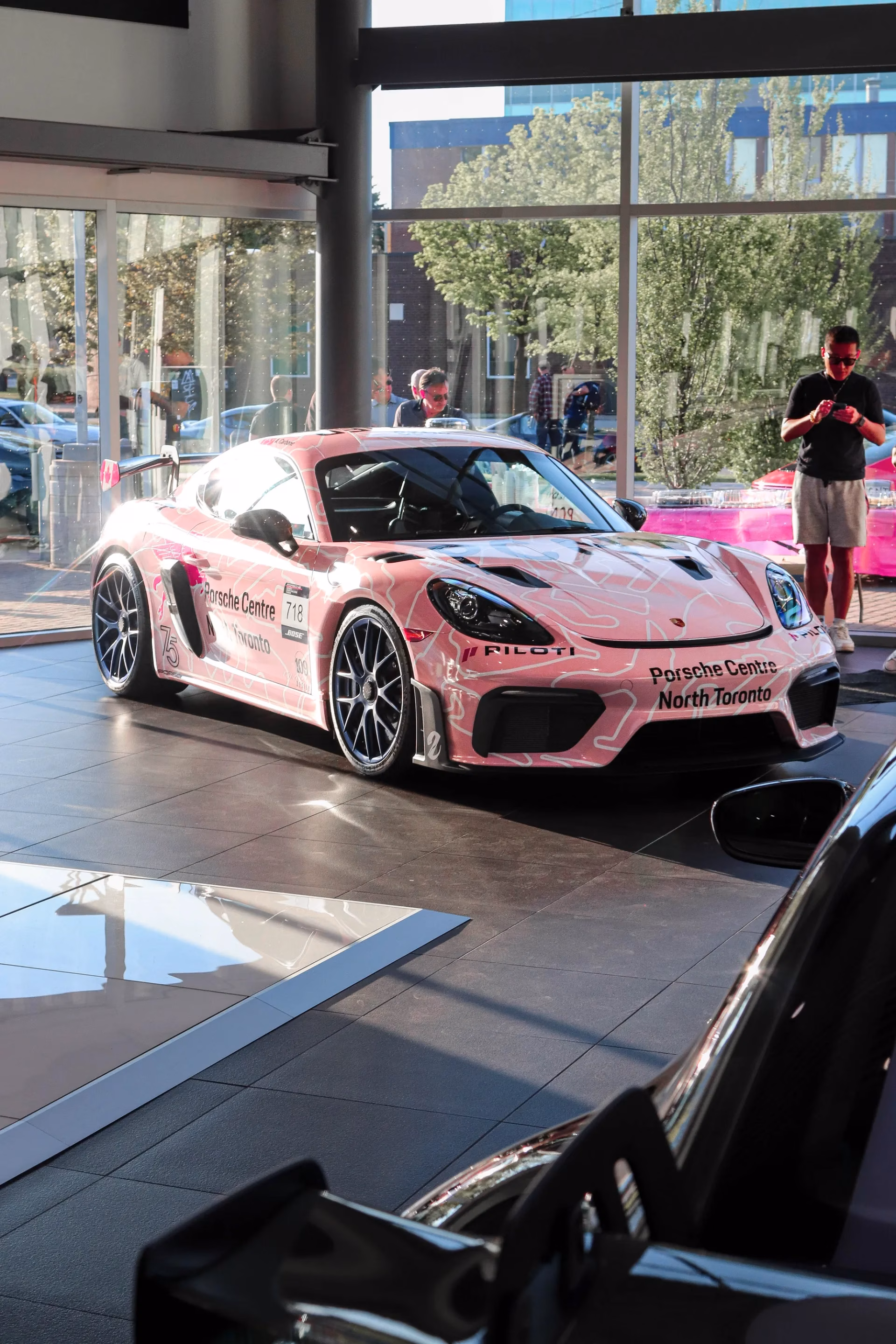 A Porsche Cayman in pink Porsche Centre North Toronto race livery on a showroom floor