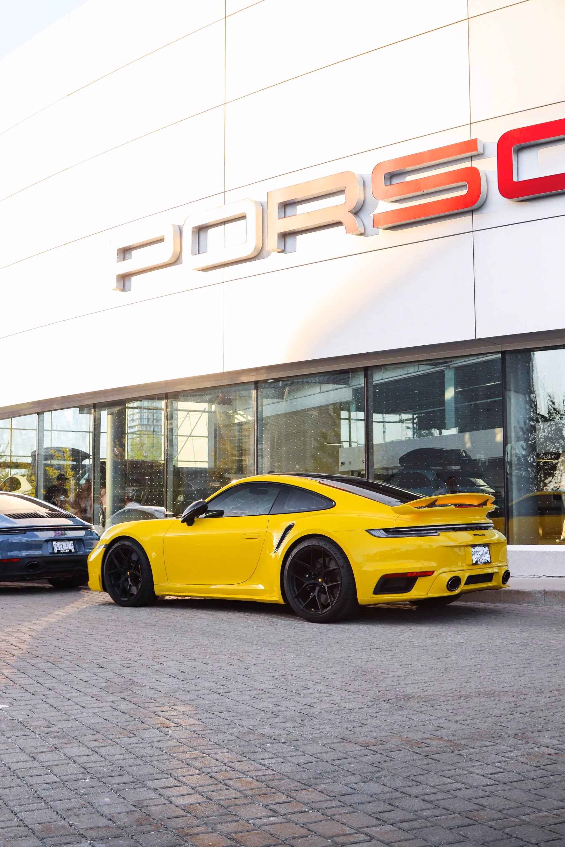 A yellow Porsche 911 parked outside a Porsche dealership