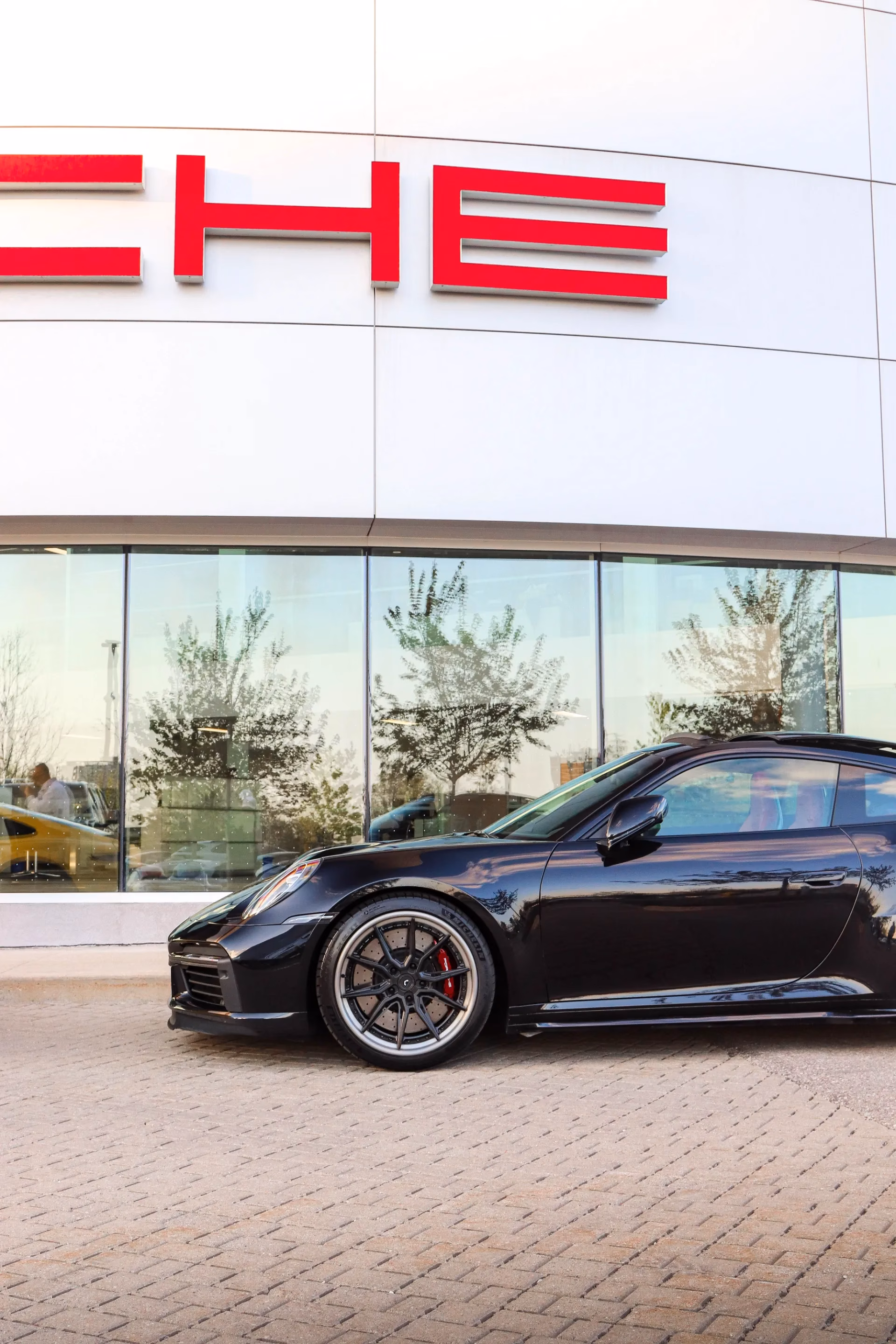 A black Porsche 911 parked in profile beneath a Porsche dealership sign
