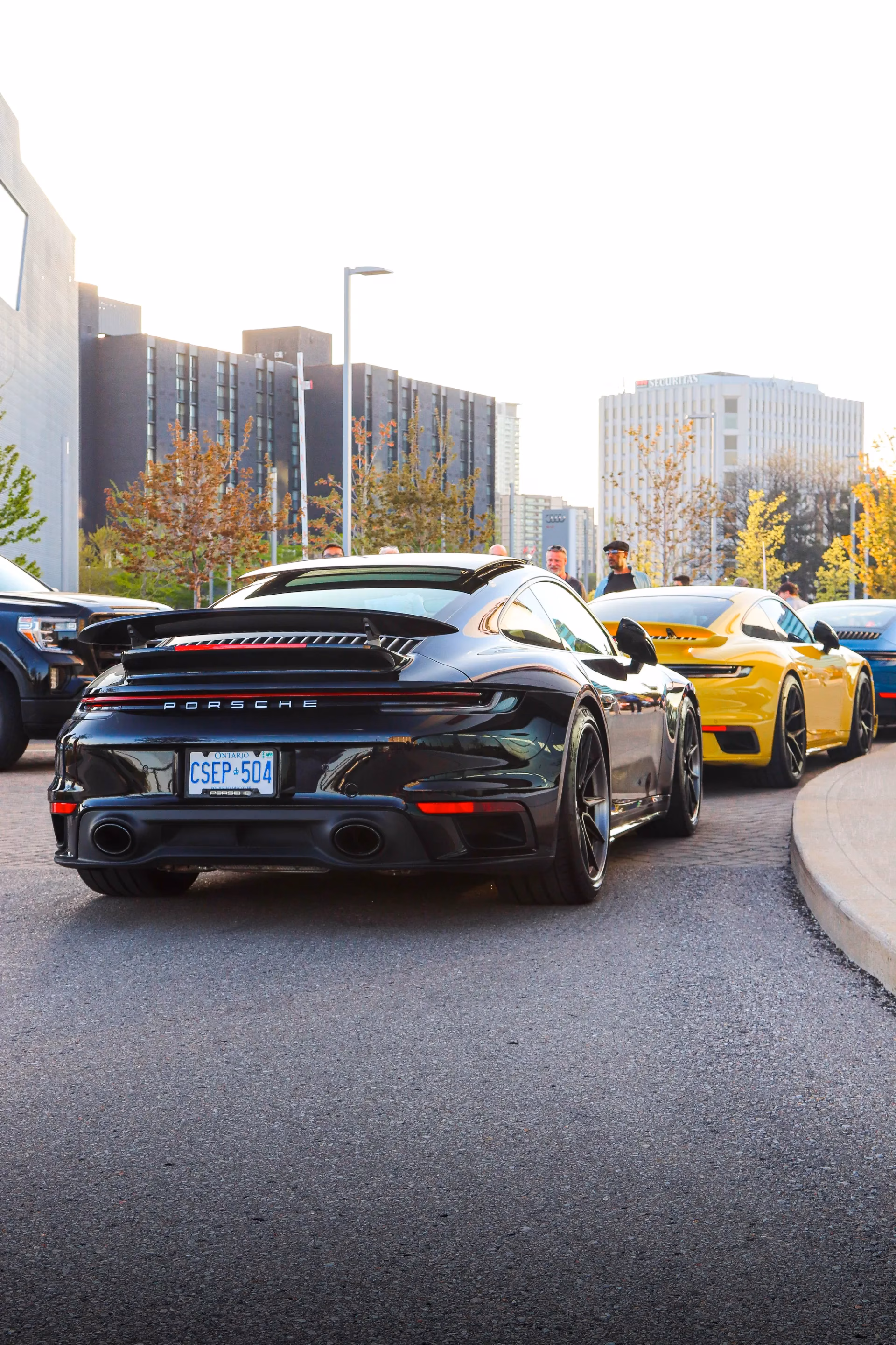 A black Porsche 911 at an autumn meet, a yellow Porsche parked alongside