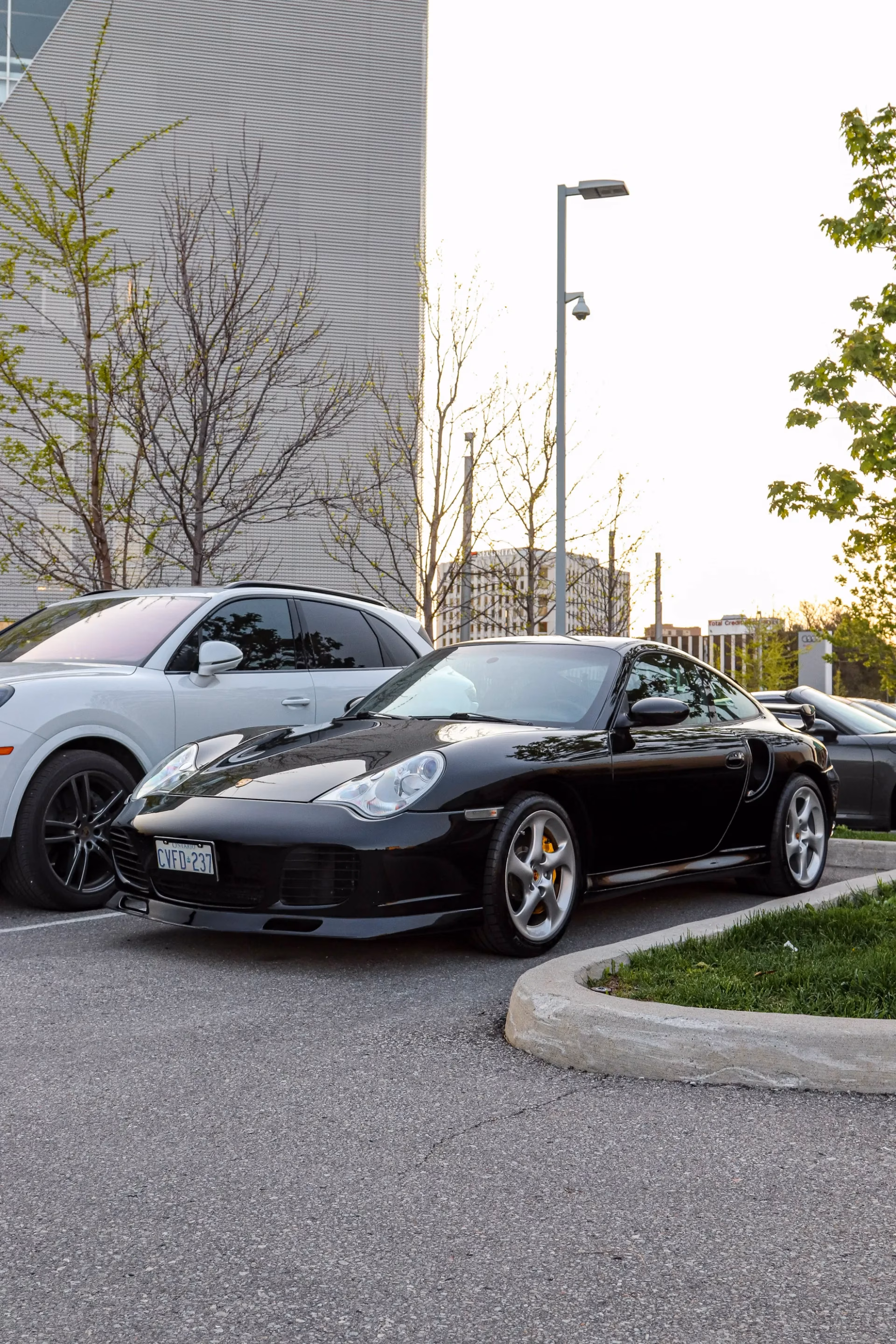 A black Porsche 911 parked at dusk beside a white SUV